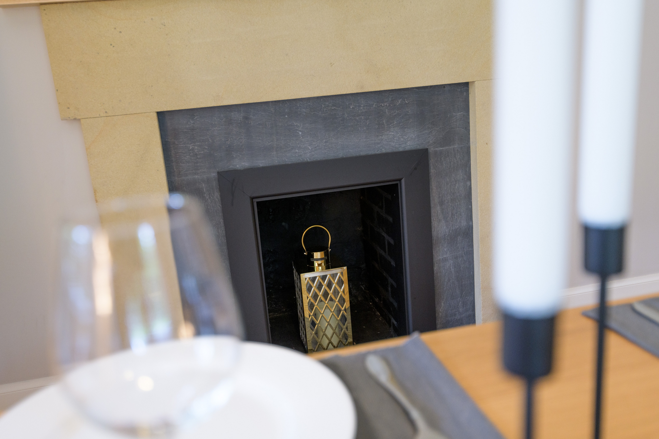 A fireplace with a grey surround, and a candle in the centre inside a gold lantern