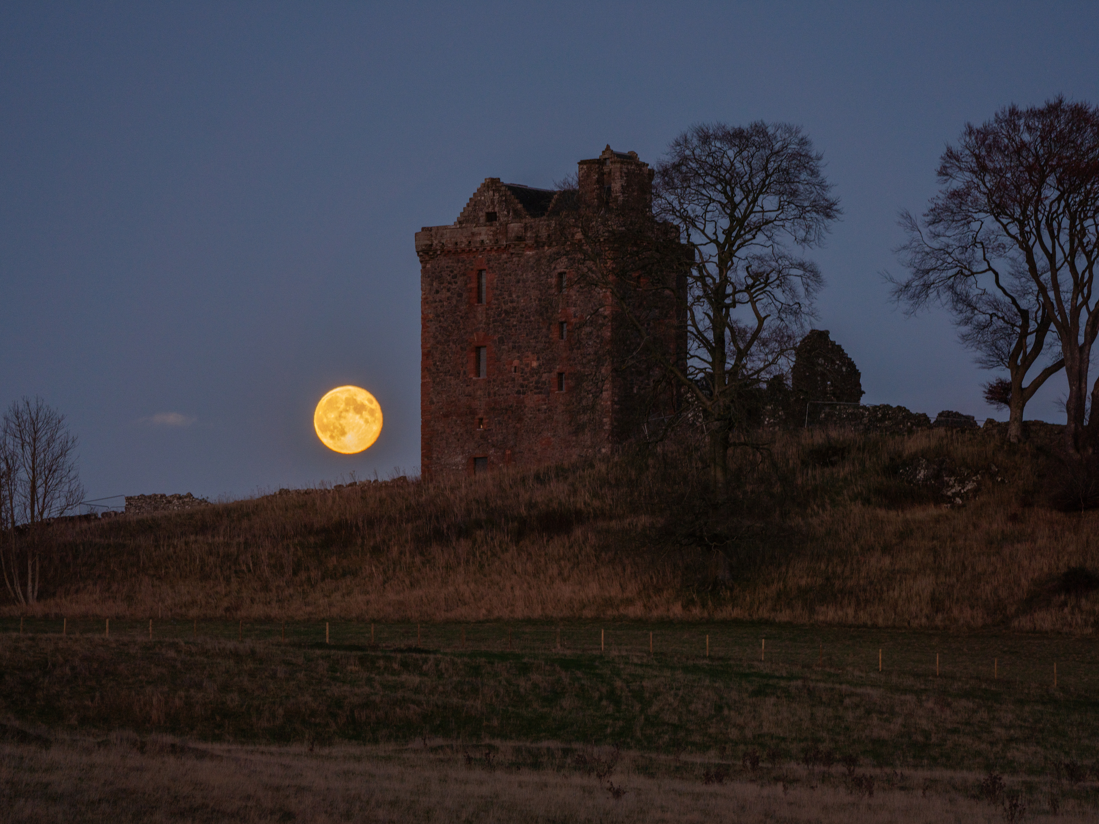 An atmospheric photo of a bright round supermoon behind a tower house