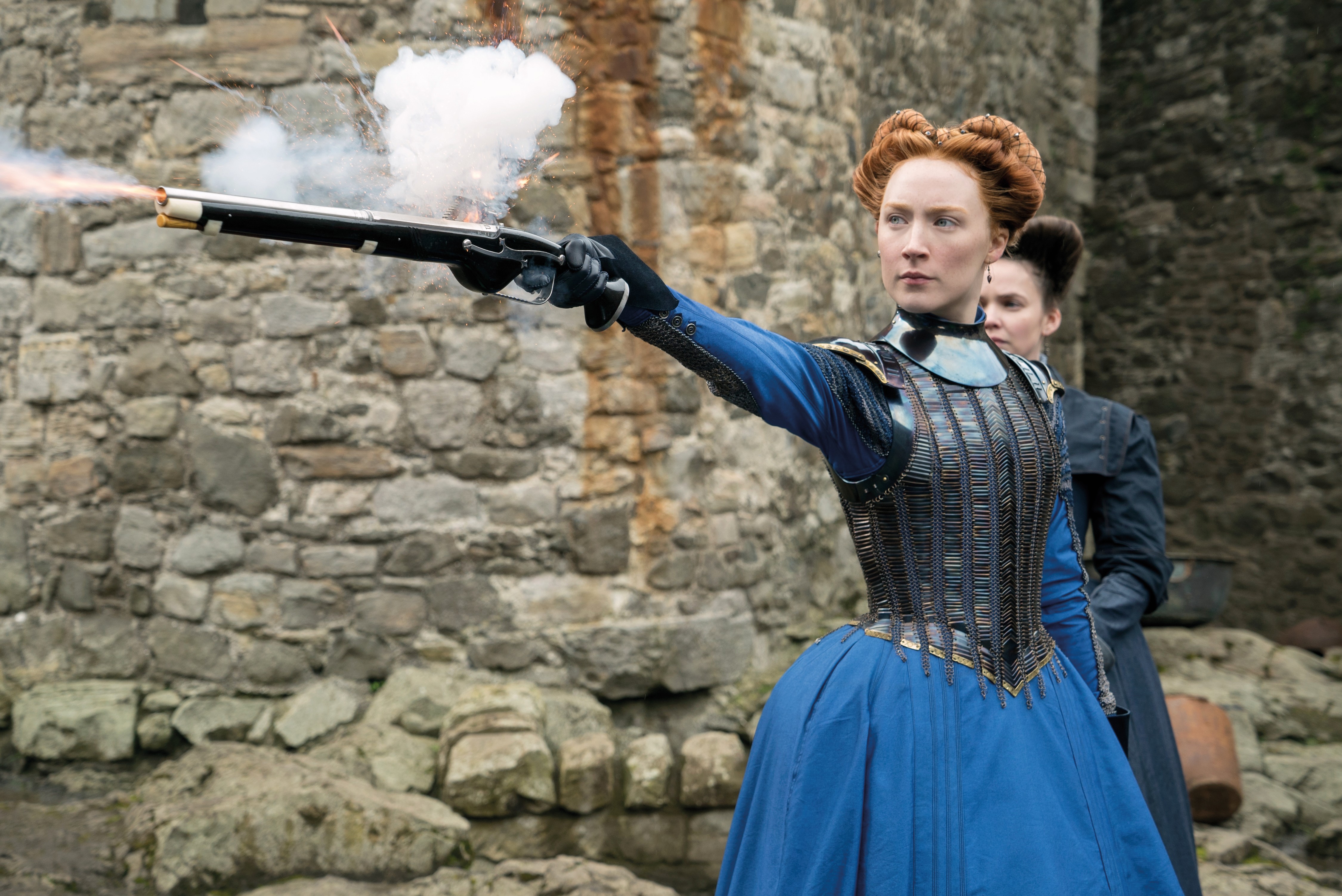 A woman in a blue historical dress fires a pistol, smoke bursting from the barrel, while another woman stands behind her against a stone wall.