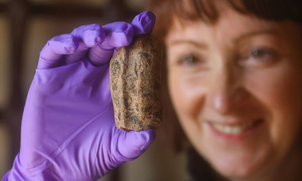 A lady wearing purple gloves holding up a  holding a pottery jug fragment from AD 400-600
