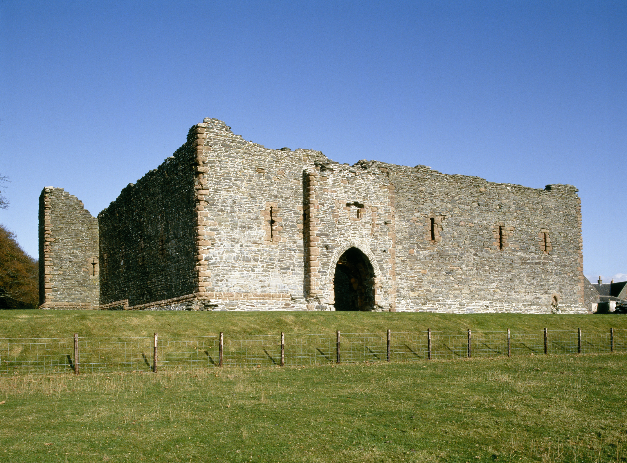Close-up view of a castle’s stone wall with an arched entryway, showing the rough masonry and red sandstone accents.