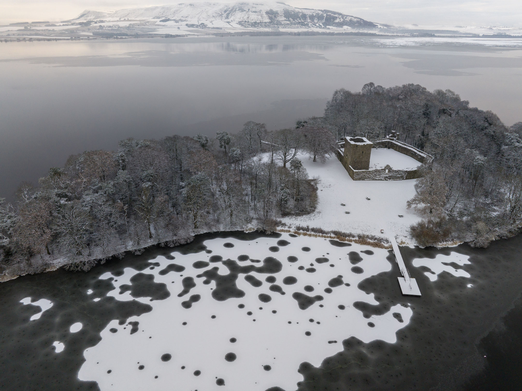 Castle on snowy island with hills and lake in background.
