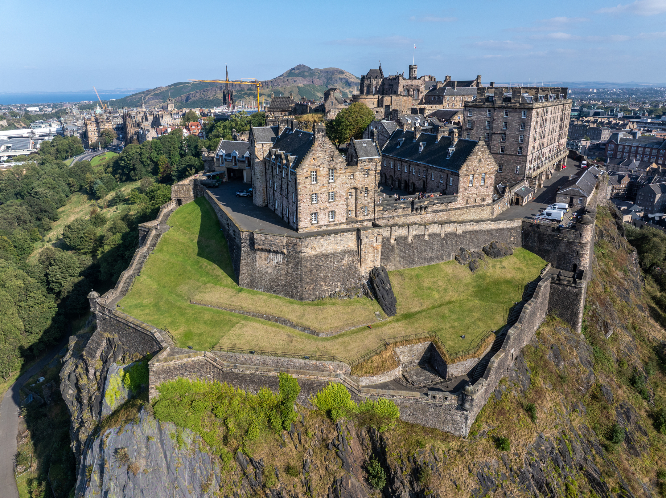 High aerial view of Edinburgh Castle complex, showing ramparts, buildings, and surrounding green slopes.