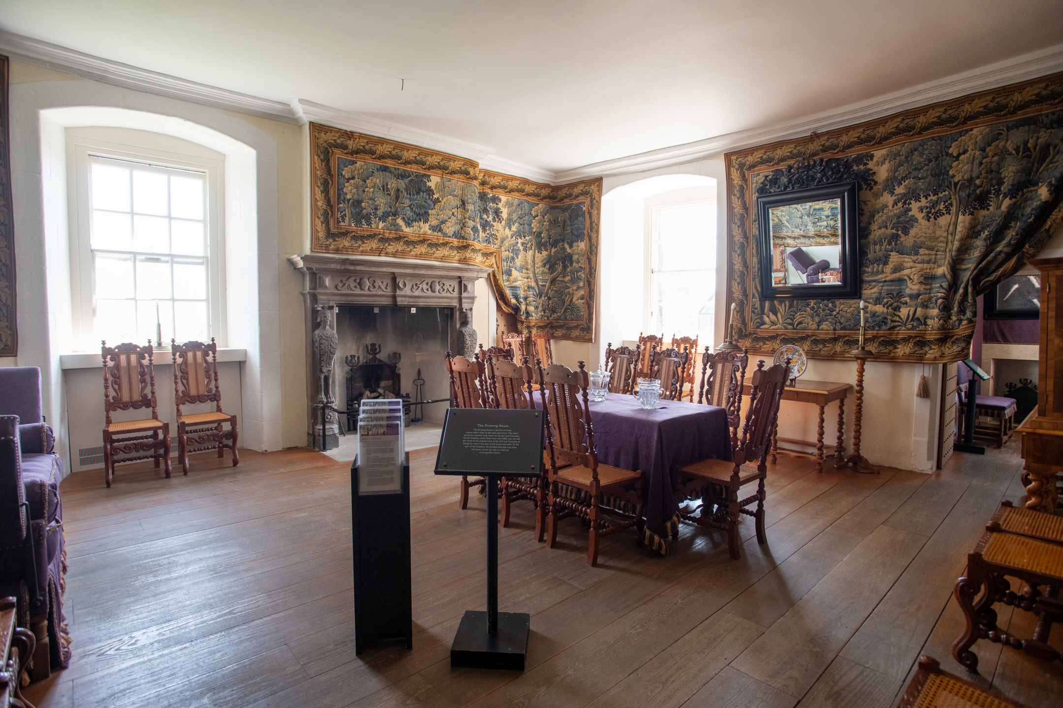 The lavish interior of a historic townhouse with a grand stone fireplace and tapestries hung on the walls.