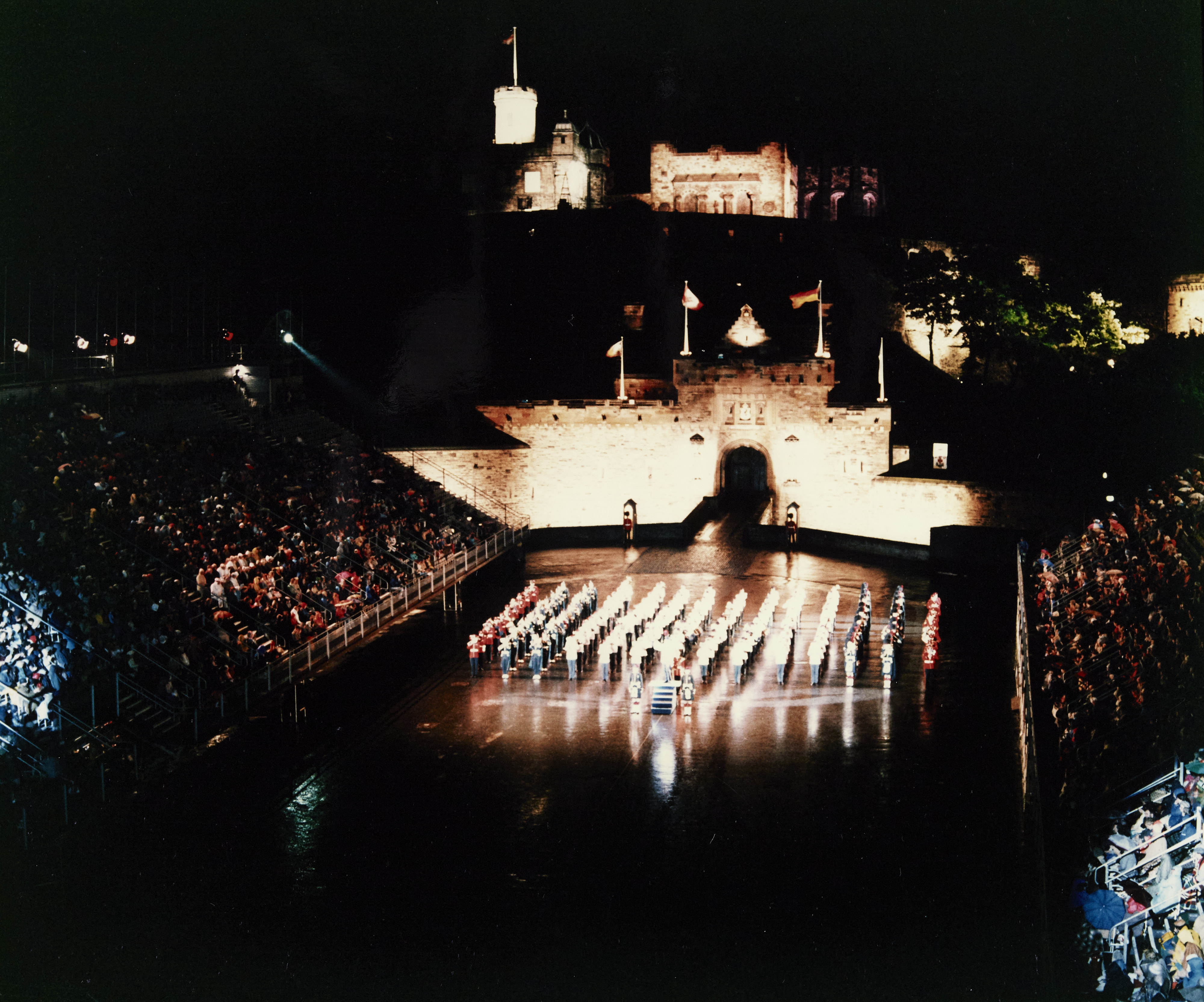 Edinburgh Castle esplanade in the dark with a military group in lines lit up in the centre, and a large crowd in the stands