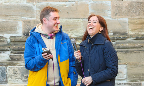 Our podcast host Sarah MacGillvray holding a microphone and talking to a man both are laughing