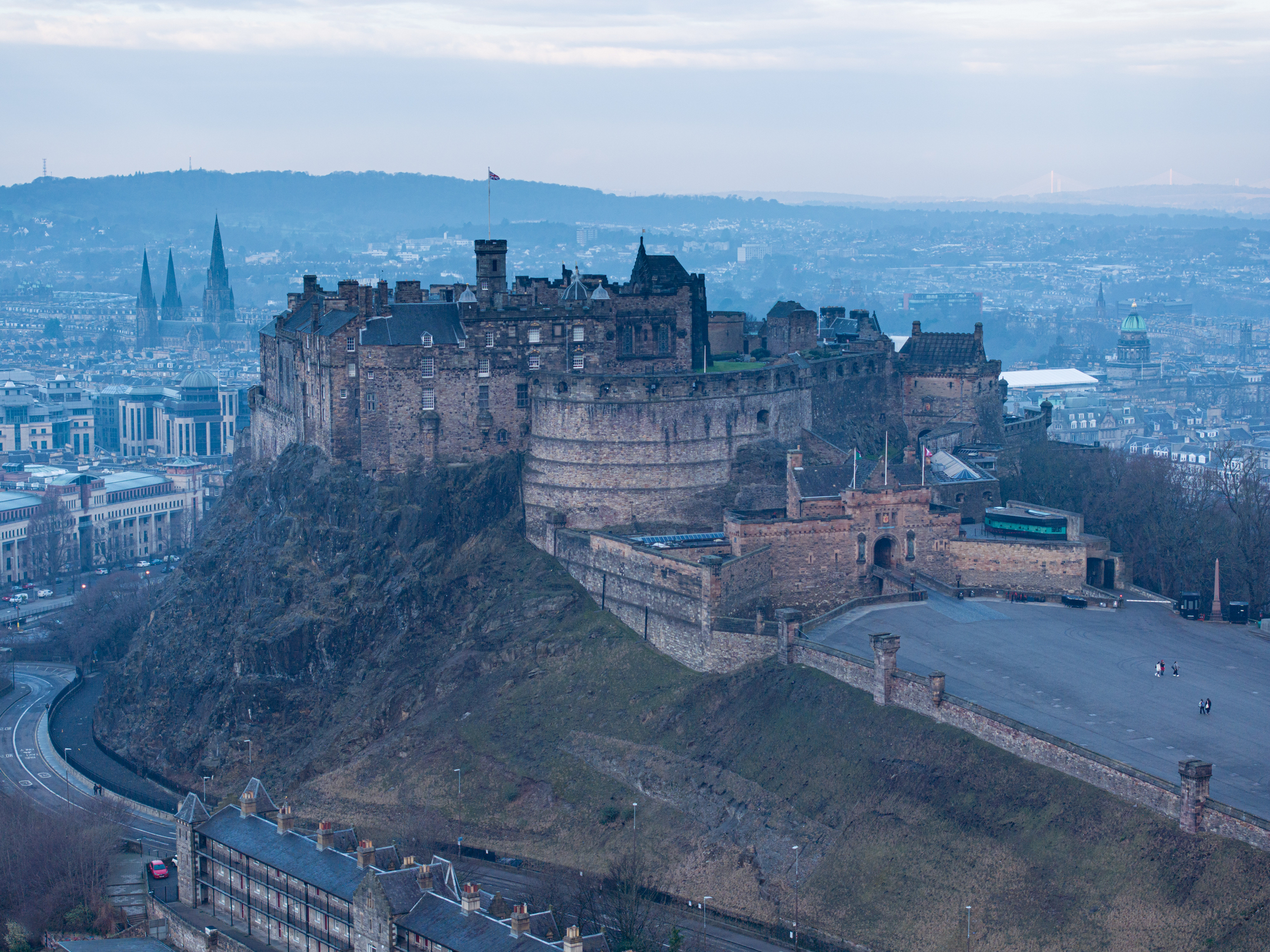 Aerial view of Edinburgh Castle and the Castle Esplanade, surrounded by city buildings and distant hills.