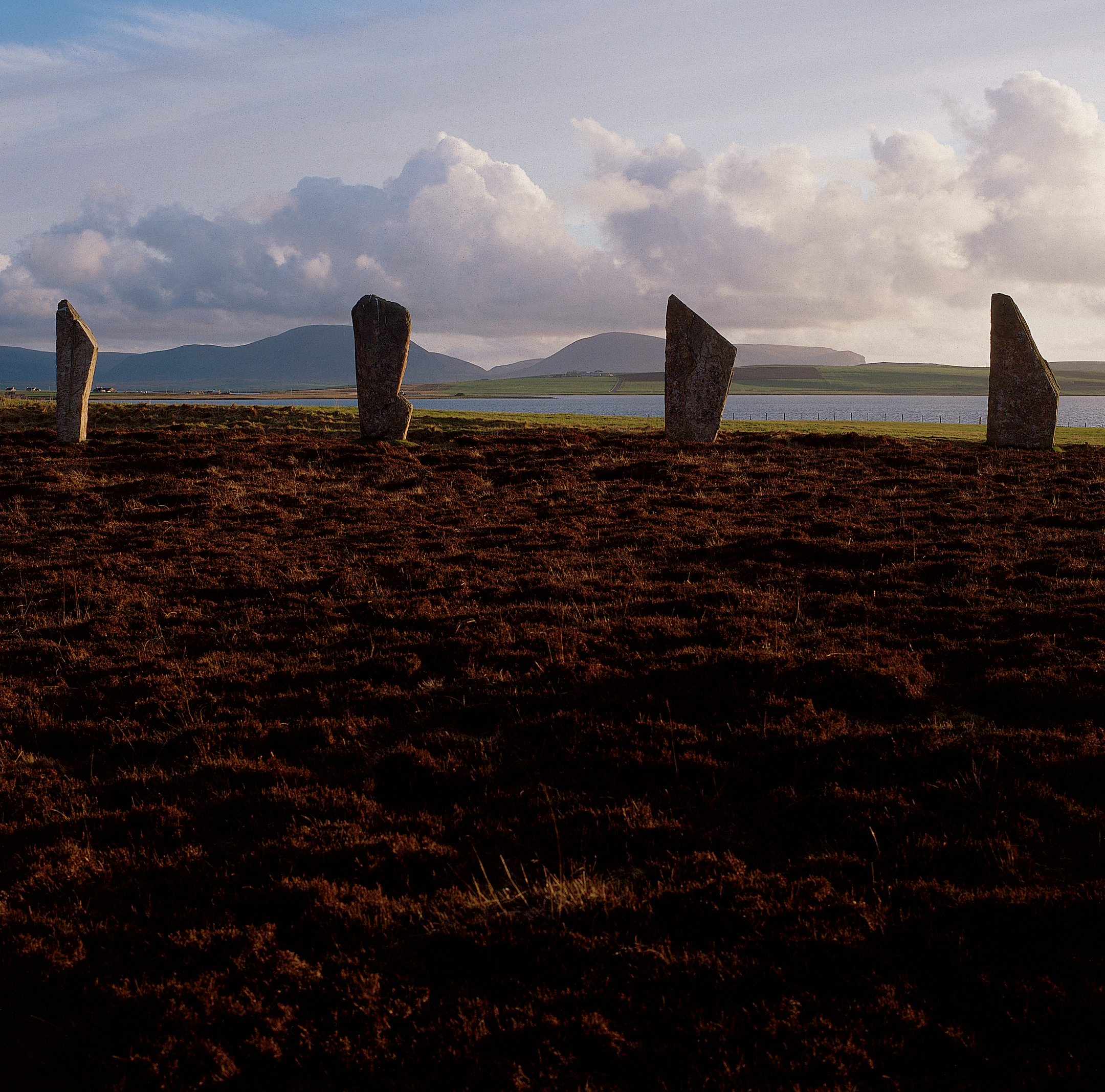 Four large standing stones on a remote moorland. They are framing distant hills and a loch or sea. 