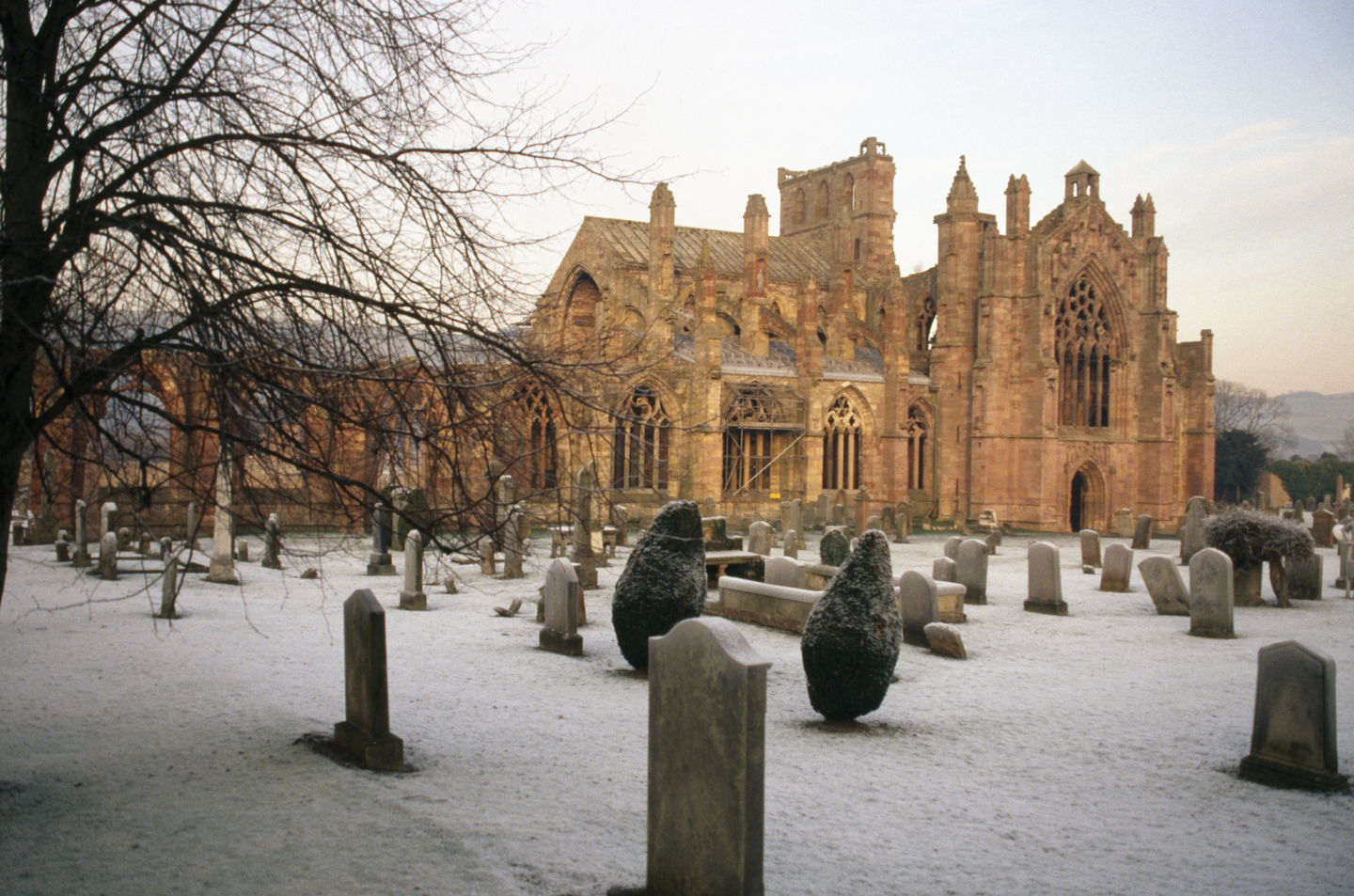 A large, stone historical abbey, in good condition. There is a graveyard in front of it, the ground has a light dusting of snow. 