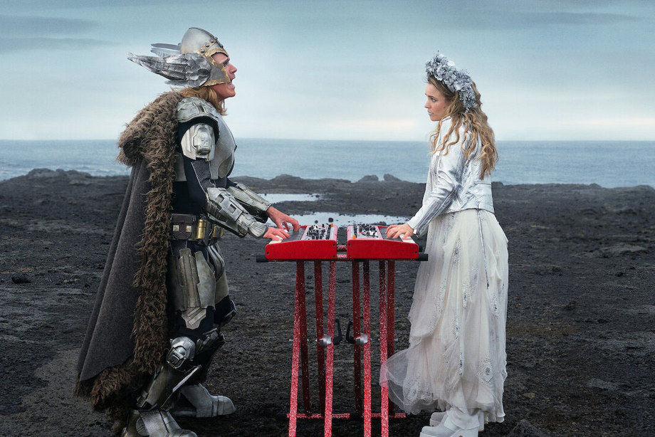 Two people dressed as Vikings both playing the keyboard on dark ground with the sea behind them