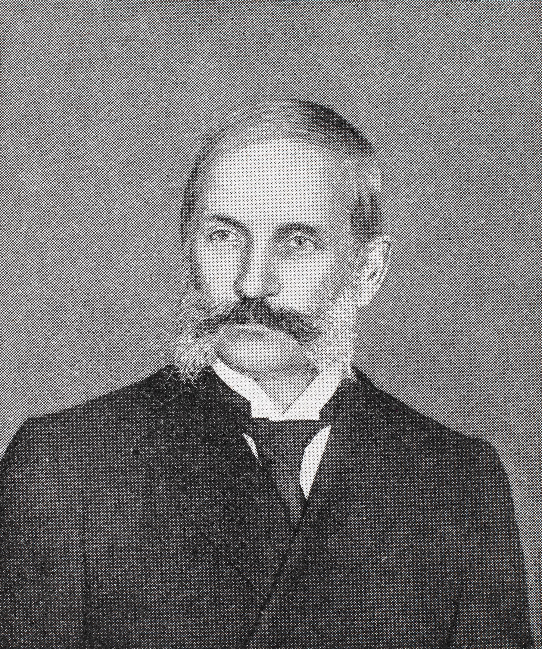 Black and white portrait photo of a young looking John Thomson from 1898. Thomson has a mutton-chop style beard, with his long dark moustache joining up with even longer white sideburns. He is wearing a dark suit, with a white shirt and tie.