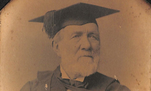 Old portrait image of David Robertson. He has a white beard and is wearing an academic cap and gown.