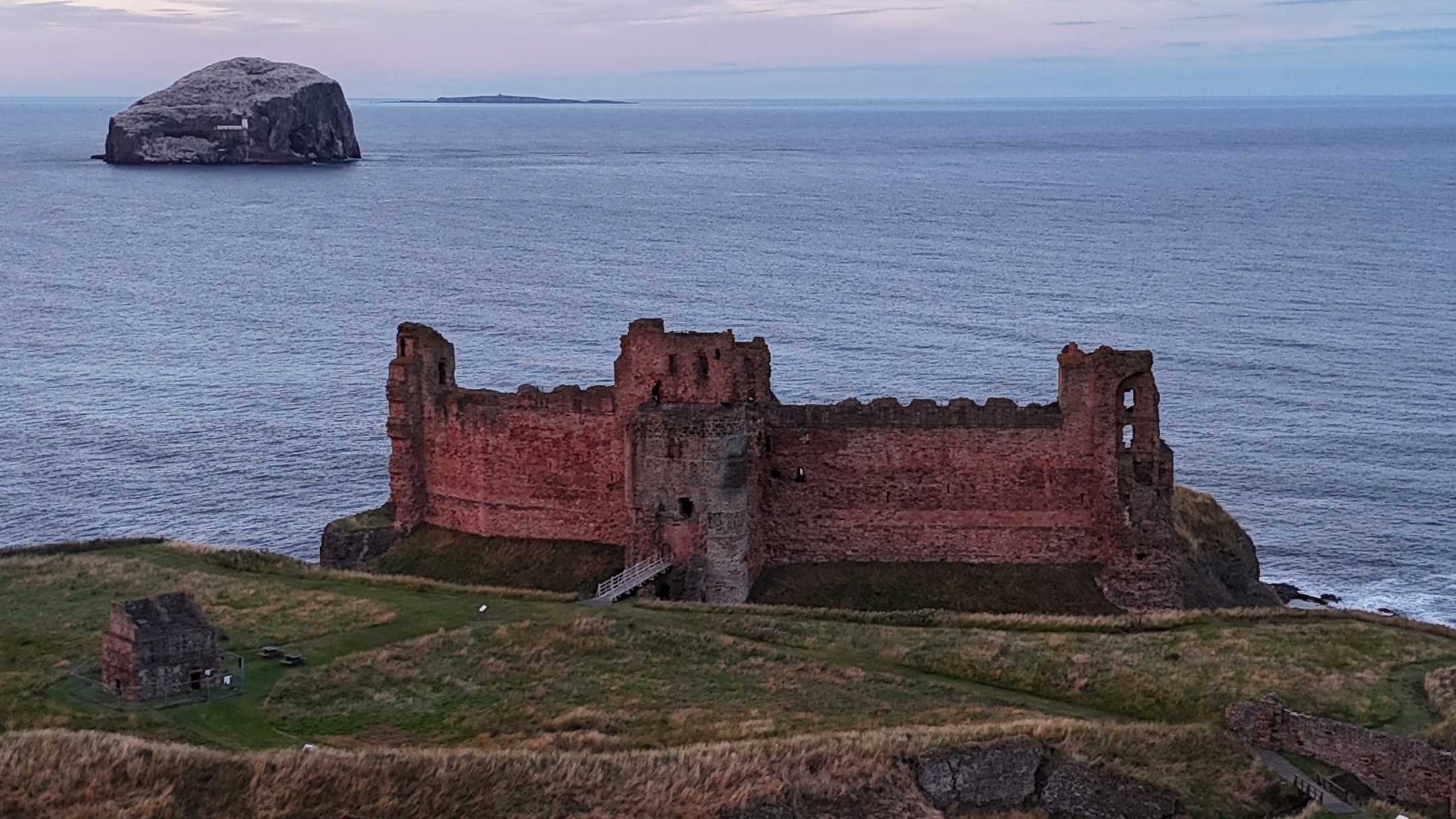Aerial view from inland showing Tantallon Castle, the sea and Bass Rock at sunset with pinkish sky