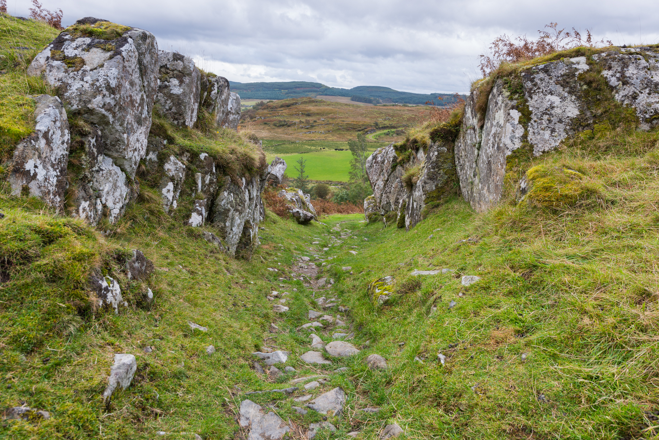 A narrow stone-studded path , leading downhill between two rugged rocky walls.