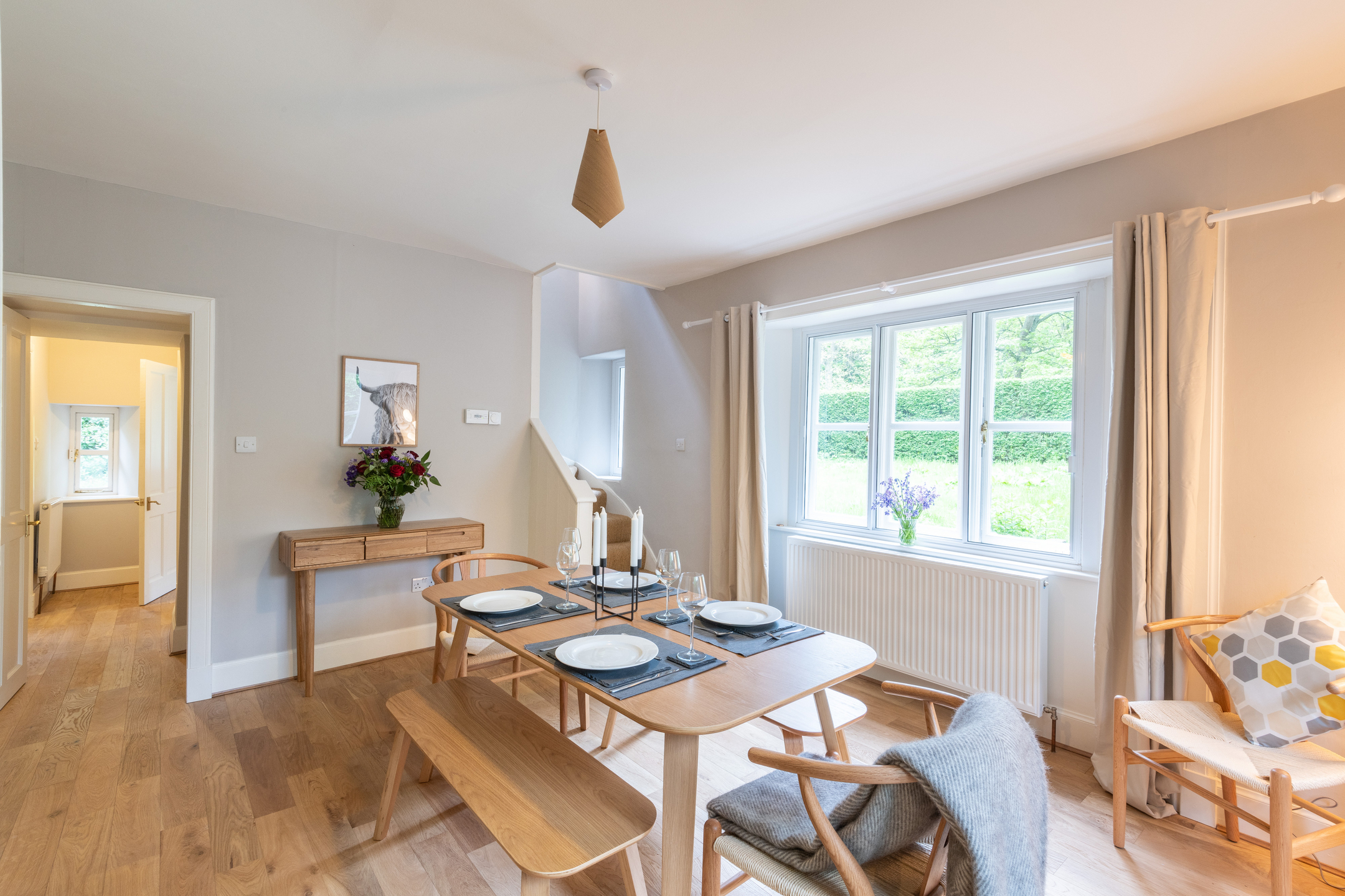 A dining room with a wooden floor and warm grey walls. There is a wooden table and chairs in the centre of the room, set with plates and placemats