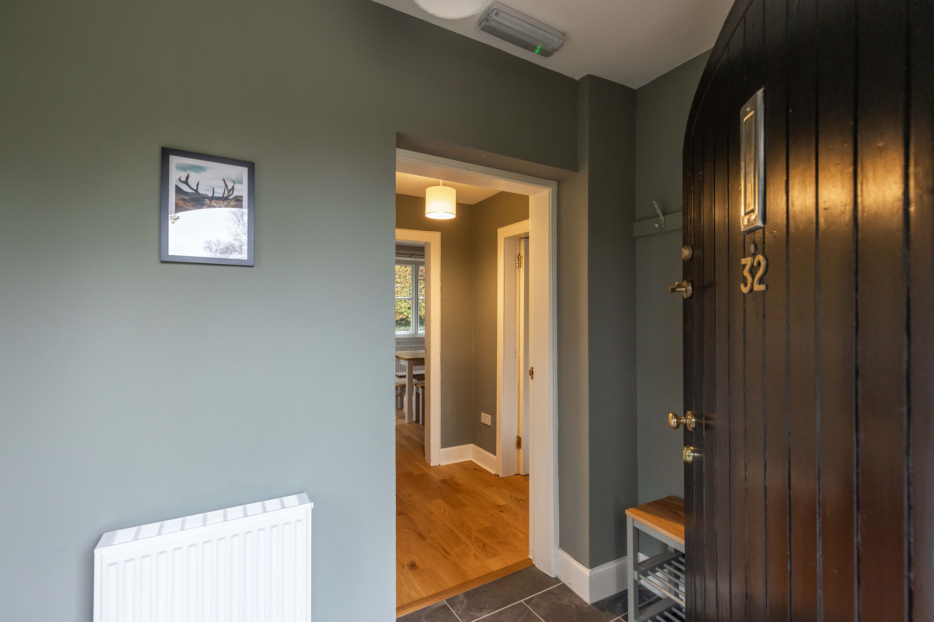 A large, black timber door opening out into a small hallway with grey walls, then opening out into a living area with a wooden floor