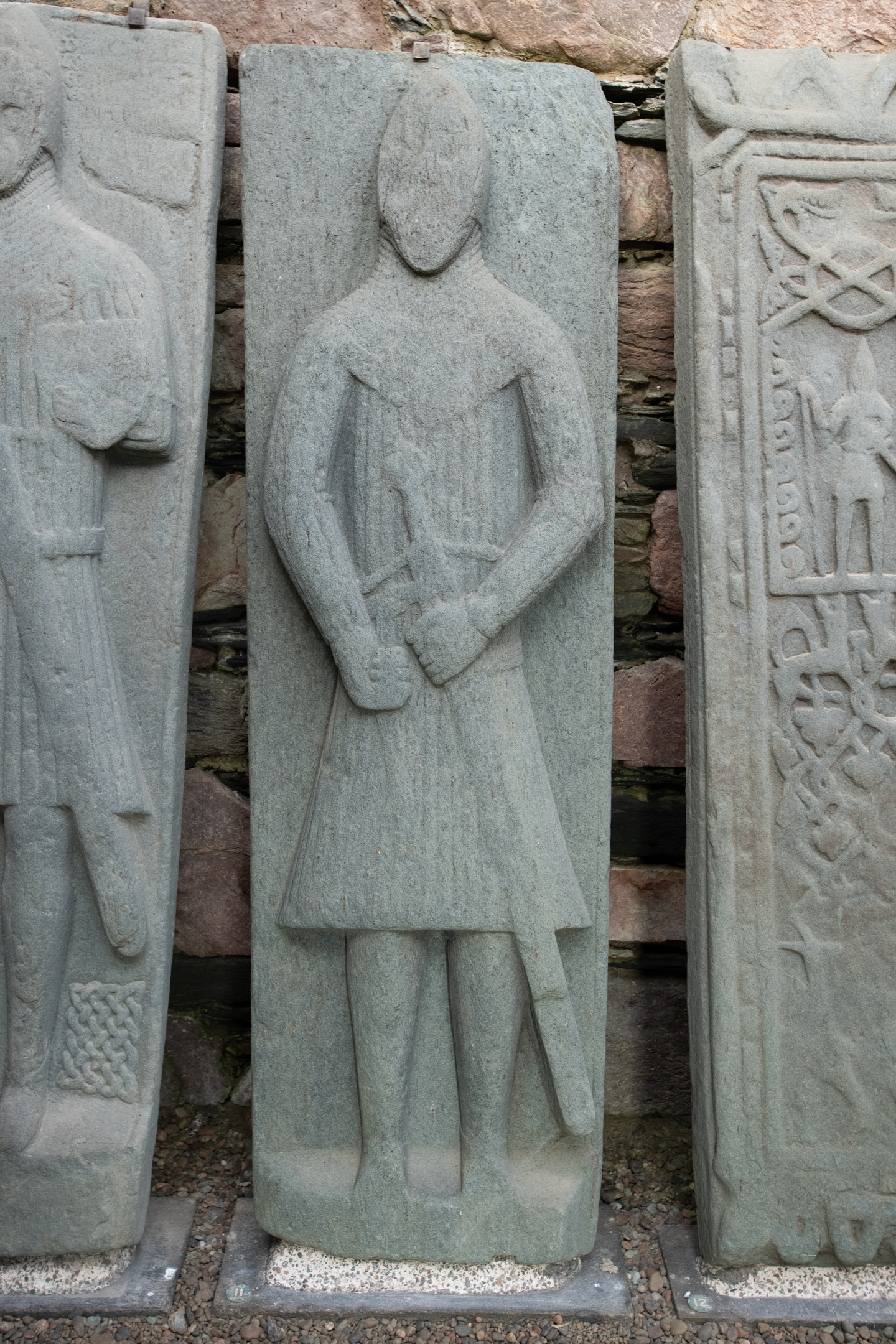 A medieval grave slab depicting a stylised figure holding a sword, carved in low relief on smooth stone.