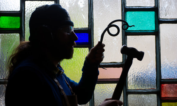 A person in front of a stained glass window holding a hammer and some iron