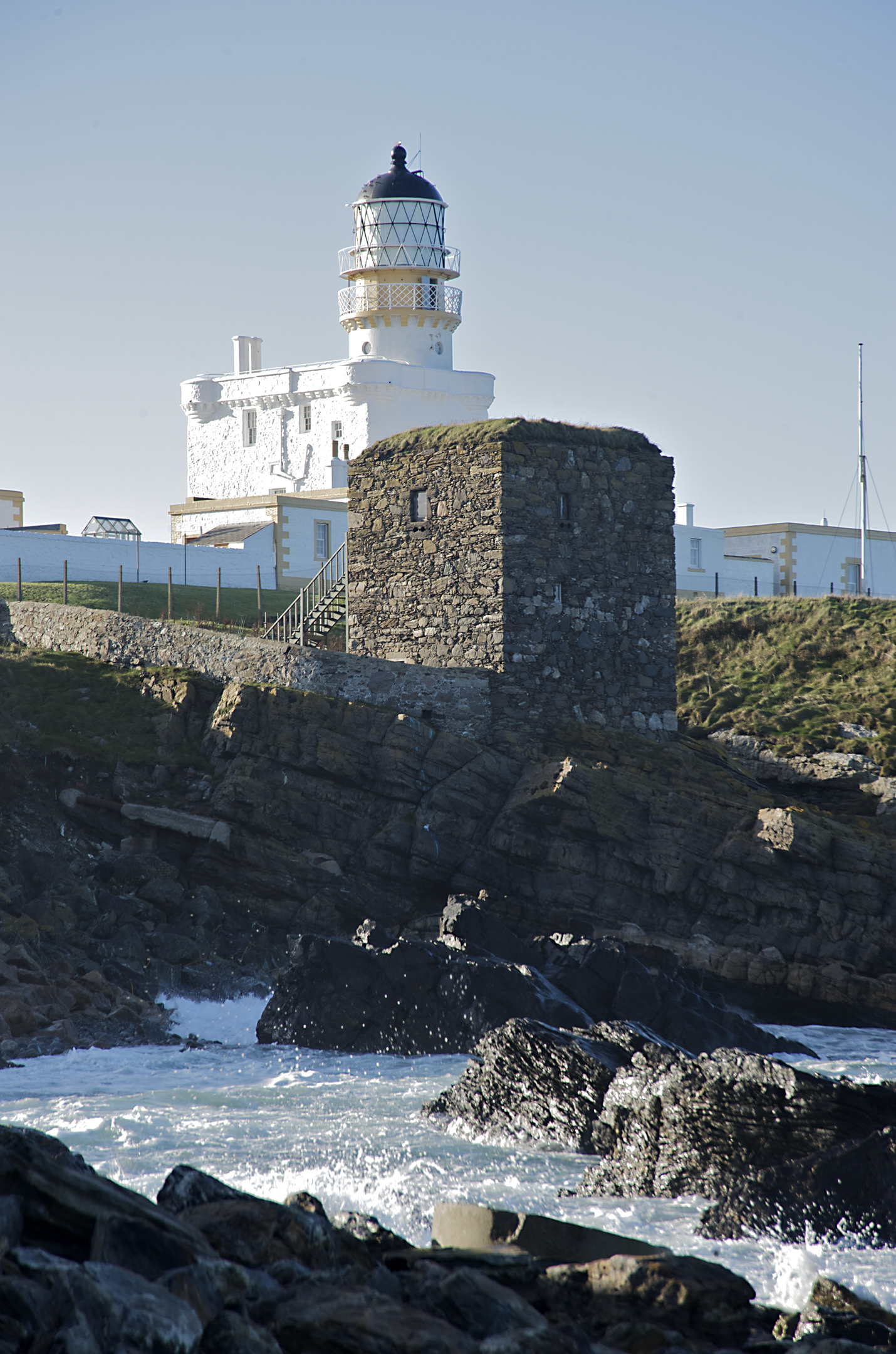 A small stone tower in front of a historic whitewashed lighthouse.