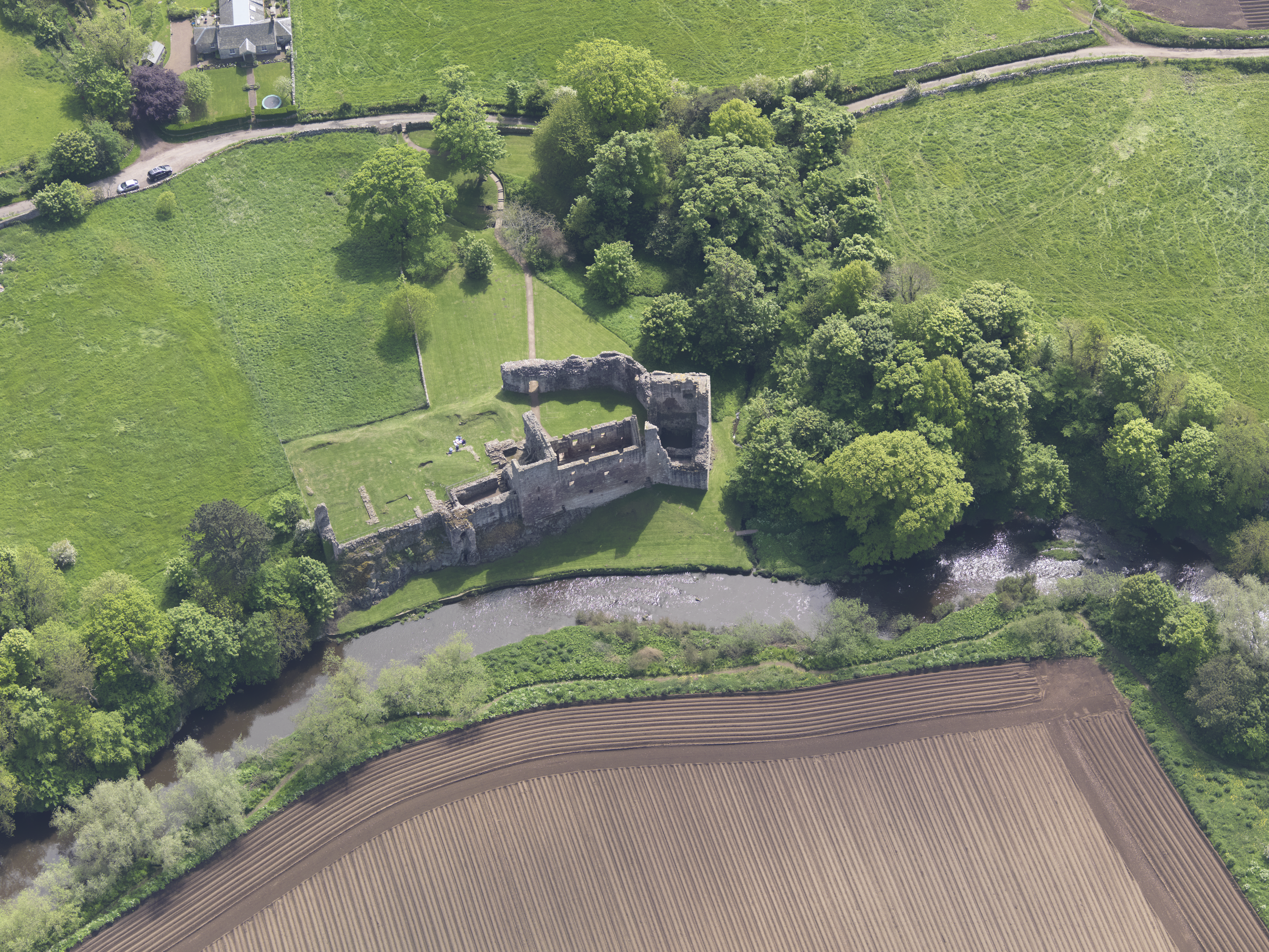 Aerial view of Hailes Castle set among green grass and trees with a river running alongside