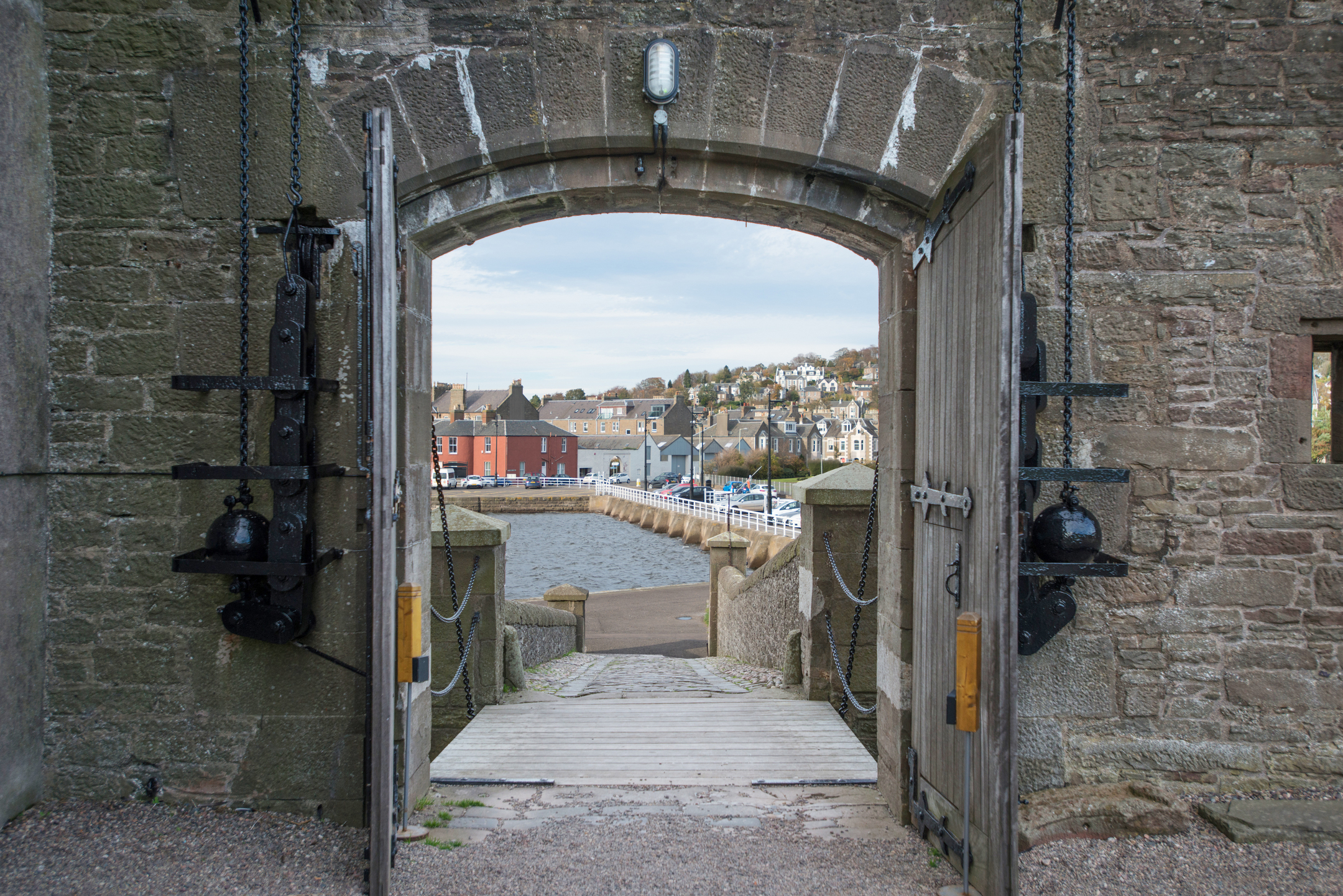 View through the open wooden gates of Broughty Castle, looking out toward the harbour and colourful buildings across the water