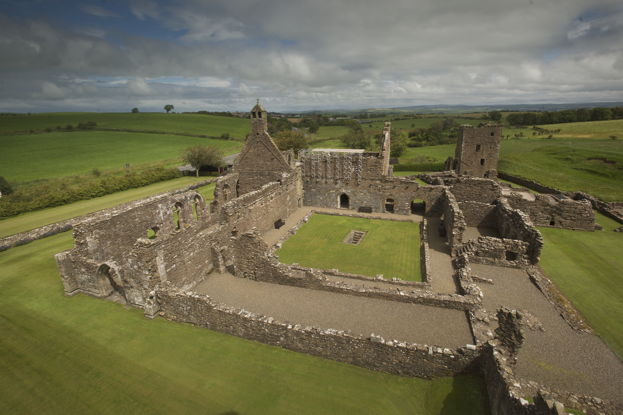 Central courtyard of Crossraguel Abbey with grass and gravel paths, enclosed by surviving stone walls and towers.