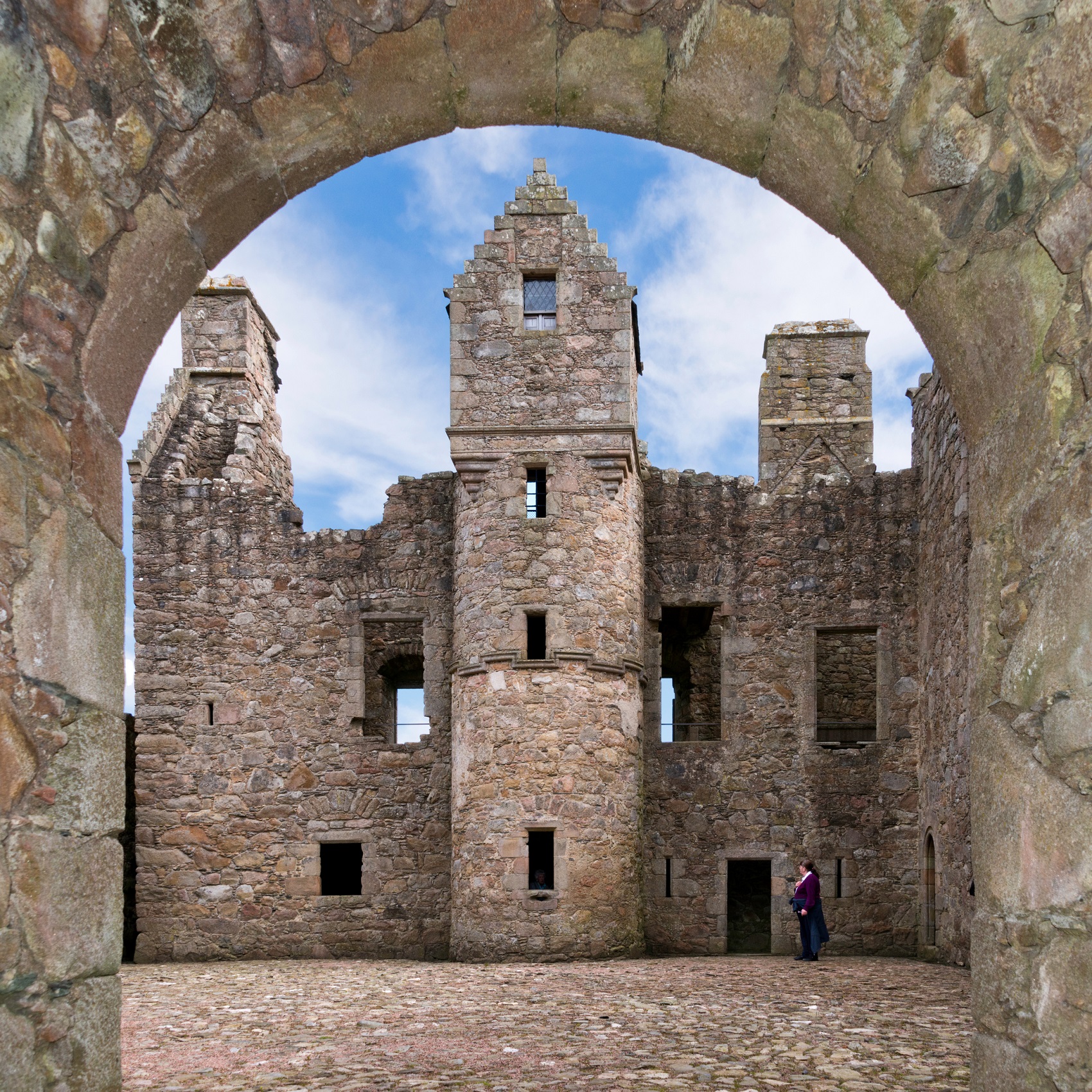 View through a stone archway into the courtyard of Tolquhon Castle, showing tall ruined walls and empty window openings.