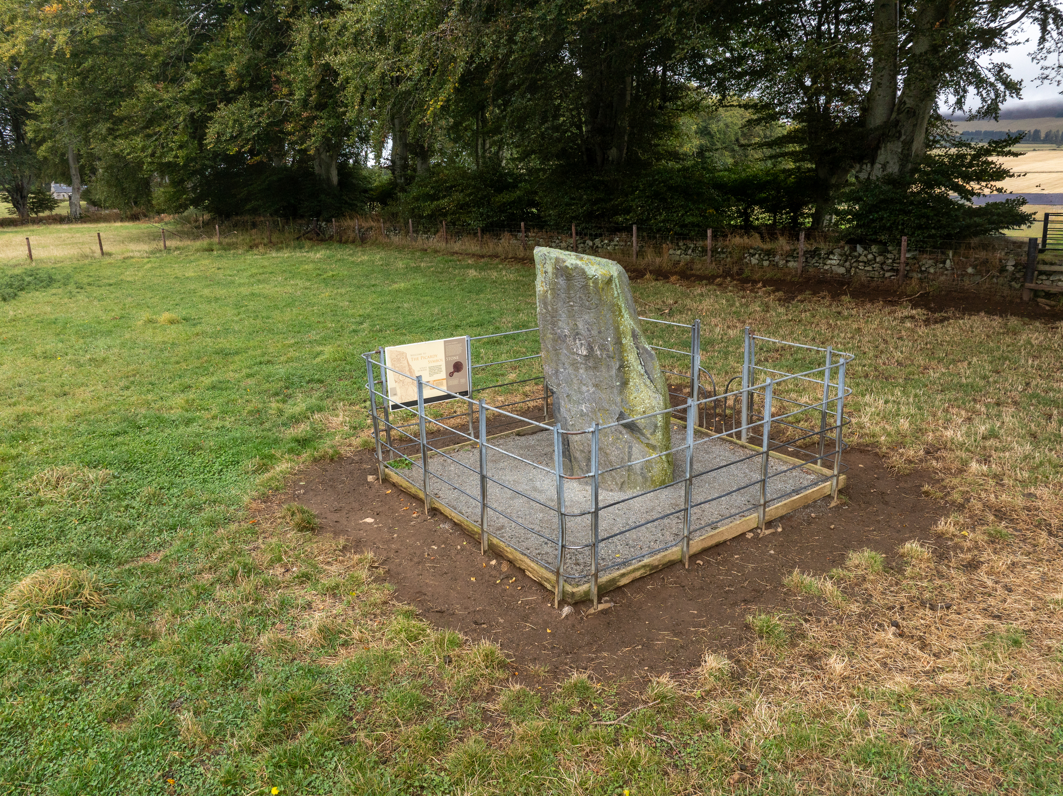 Symbol stone in enclosure and grassy surroundings with trees in background