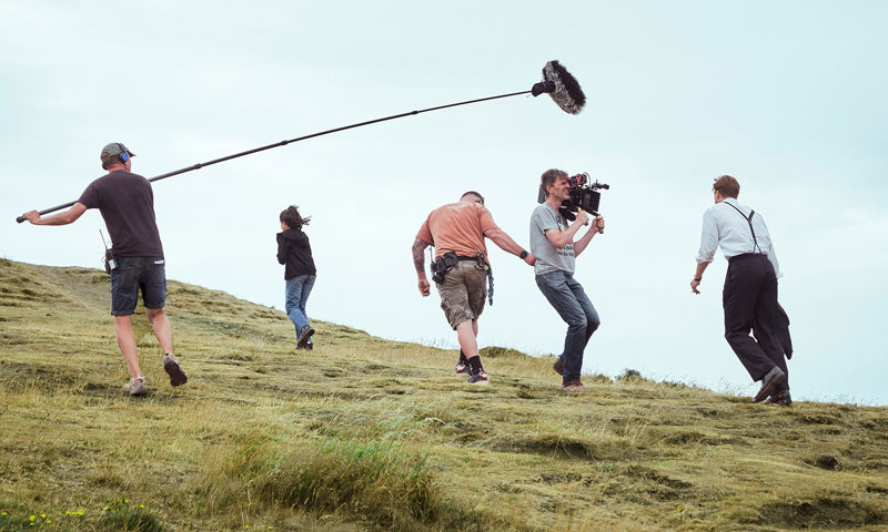 An actor walking up Arthur's Seat while being filmed by four crew members