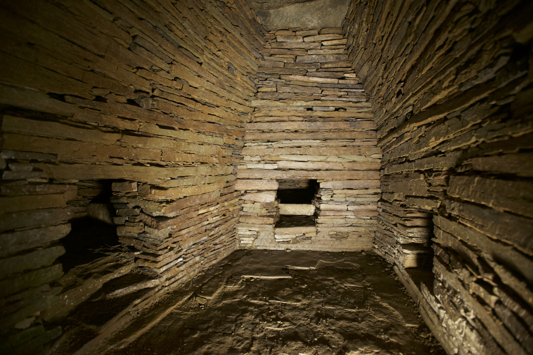 Stone-built chamber interior with side cells, corbelled walls and an earthen floor.