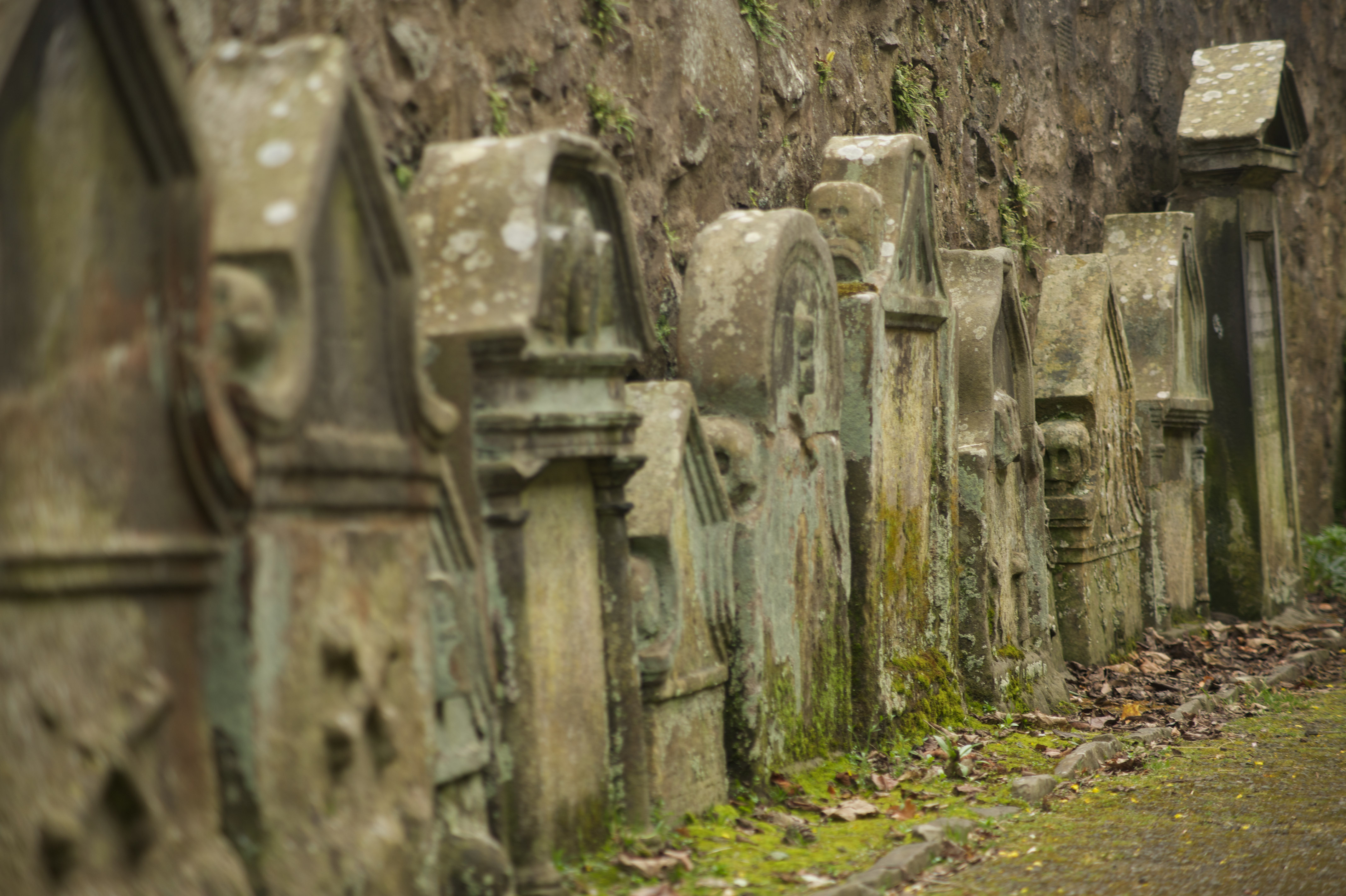 Multiple stone gravestones in a row along a high wall