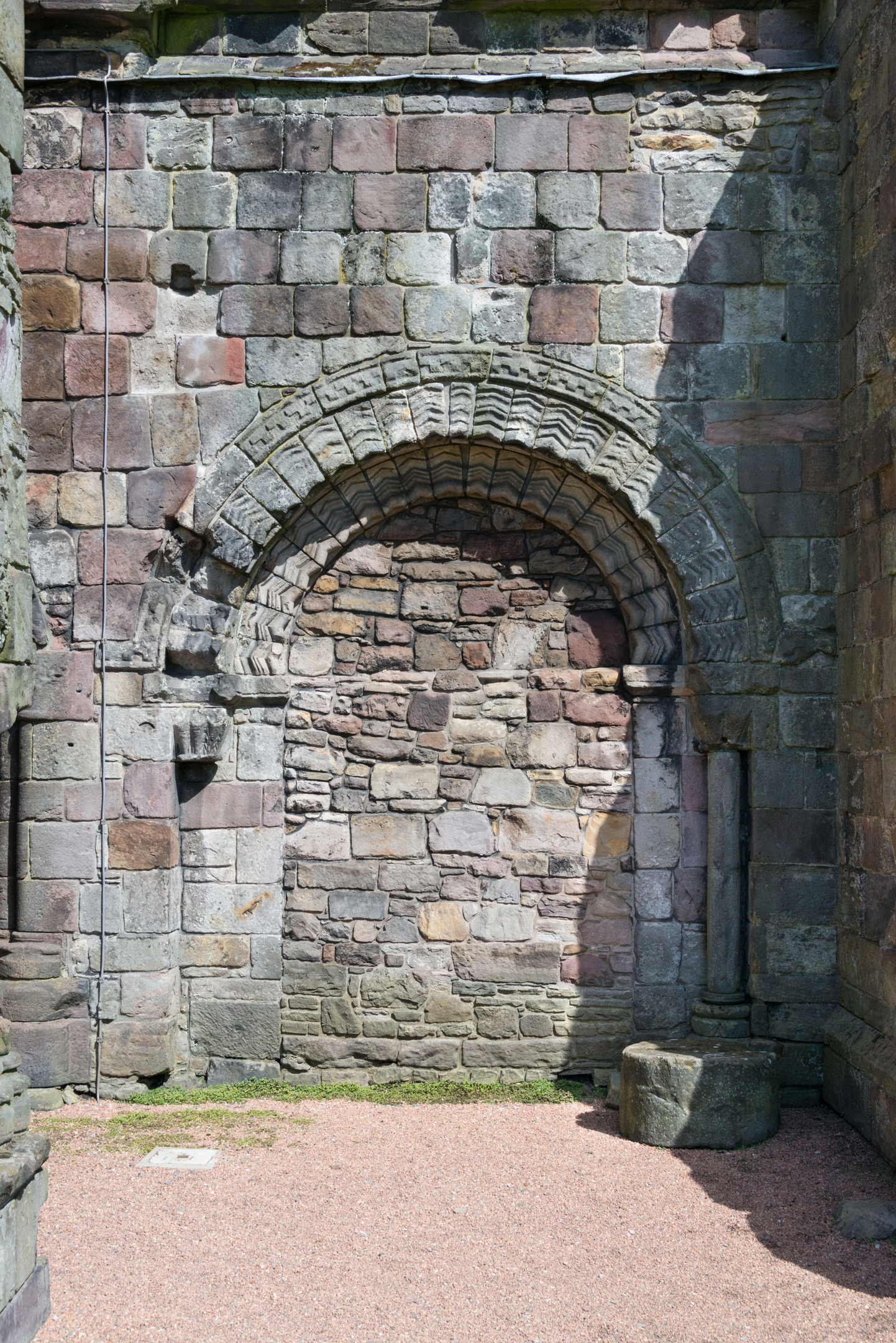 A straight on view of a Romanesque arched doorway in a wall of the nave at Holyrood Abbey. The doorway is stoned up. 