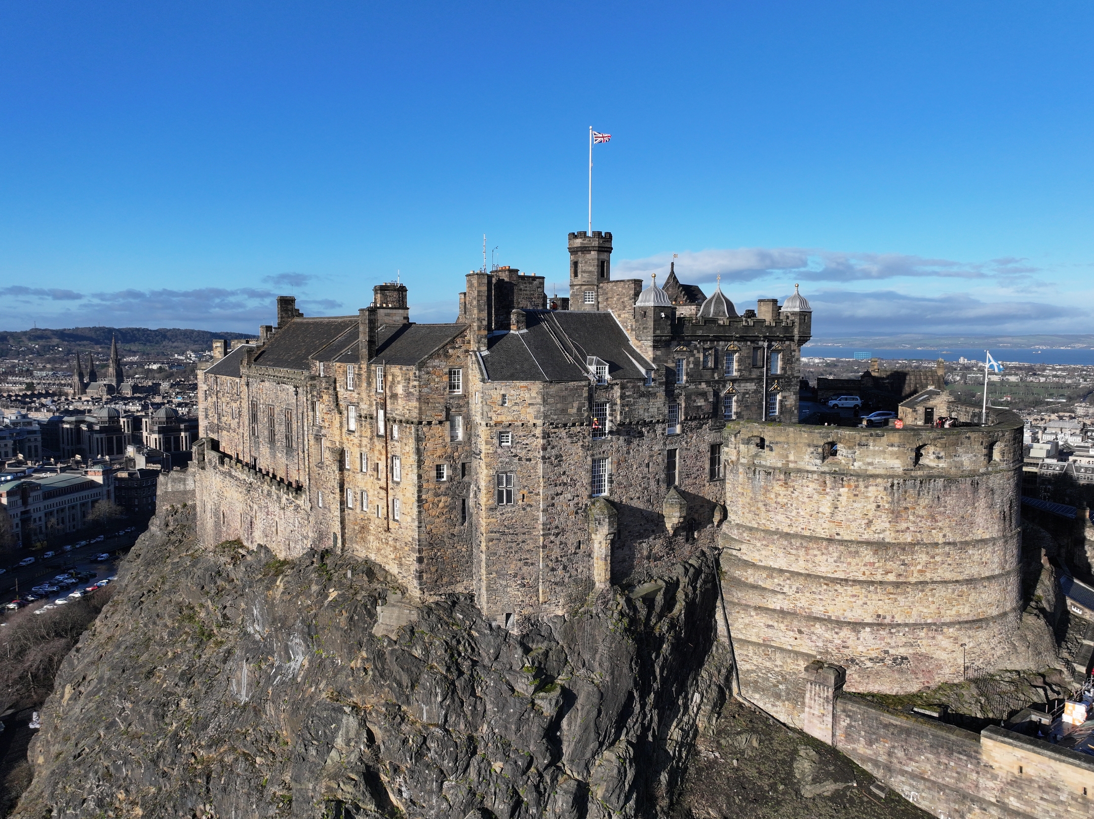 Edinburgh Castle sitting atop a steep rocky cliff, with grass-covered slopes and city streets below.