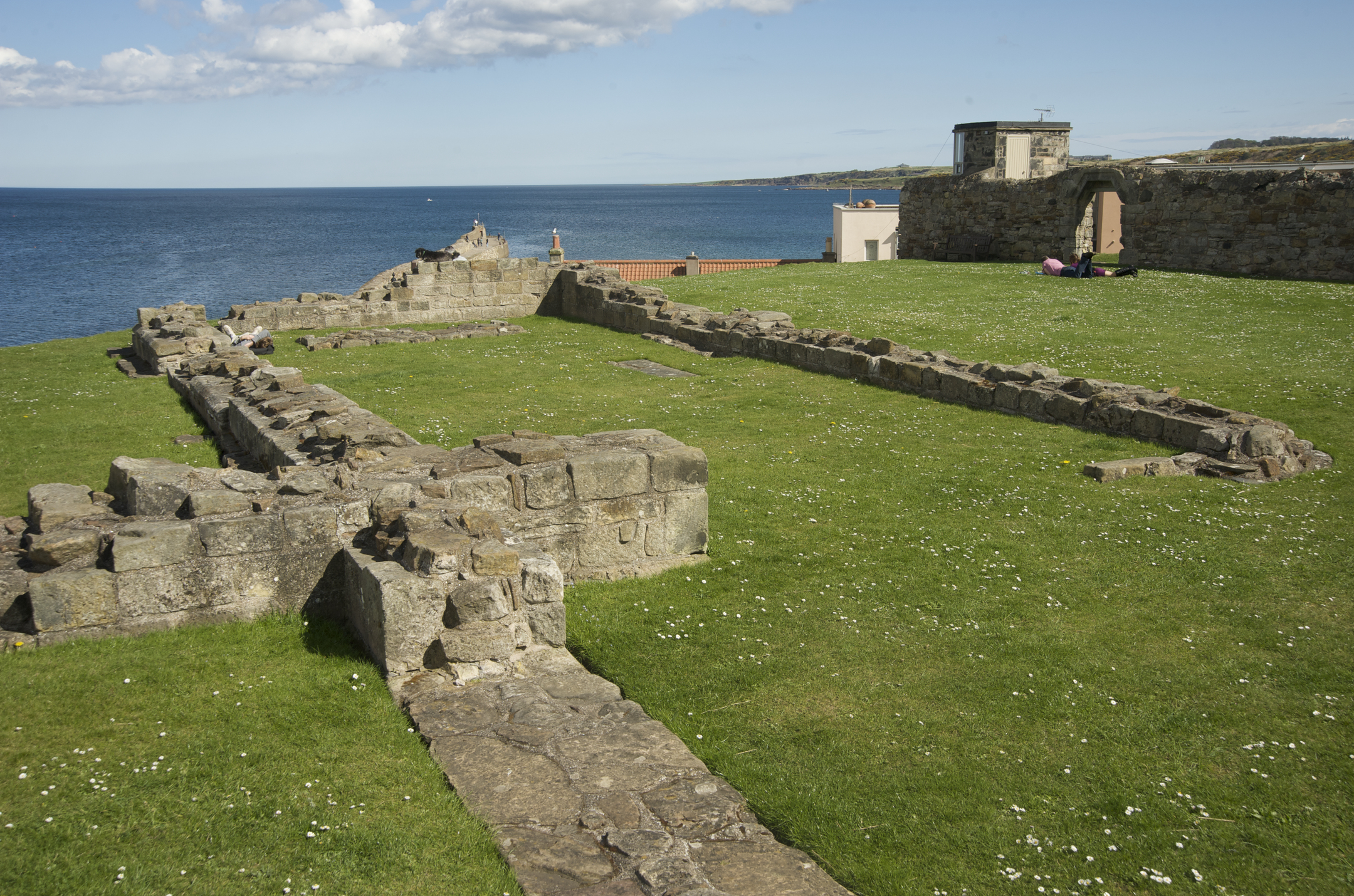 Low stone foundations of a historic church set in green grass with the sea in the distance.