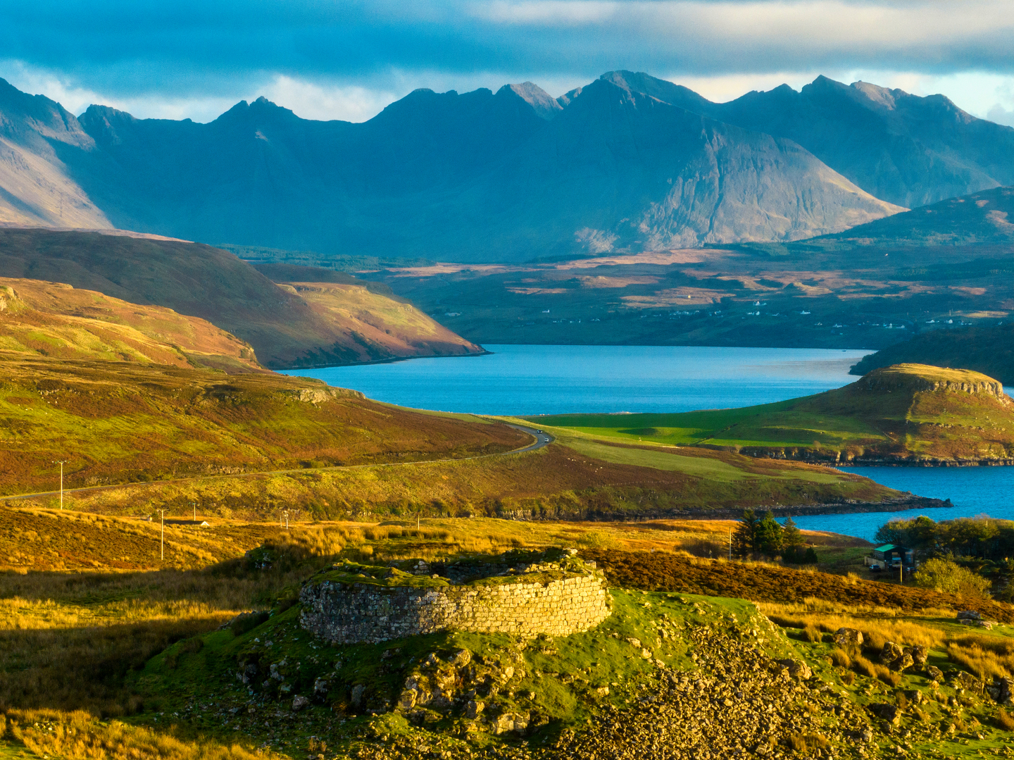 A circular stone wall on a mound, with a body of water and mountains in the background. 