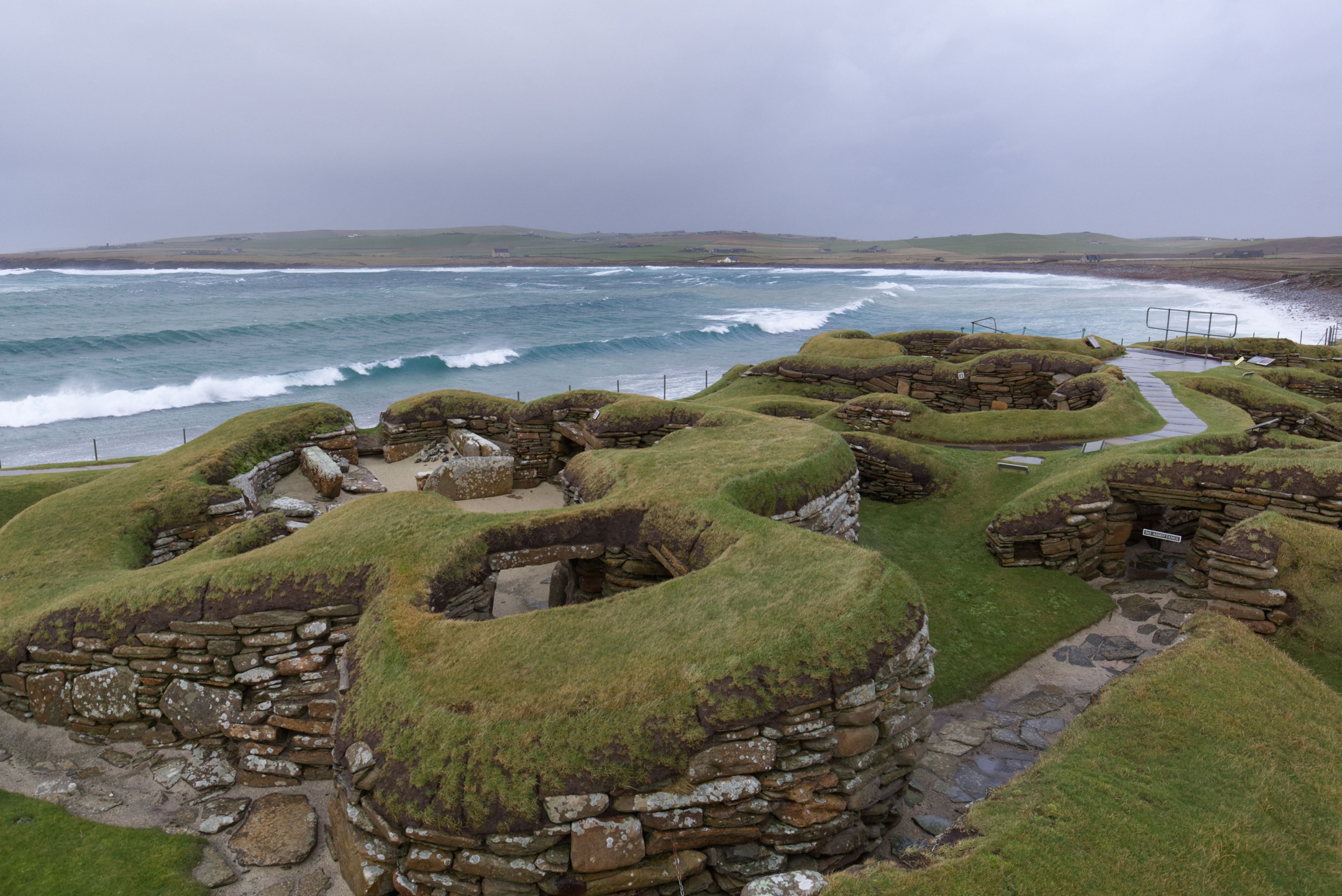 Image from the viewpoint of Structure 8 at Skara Brae, Orkney, with the storm blown coast in the background.