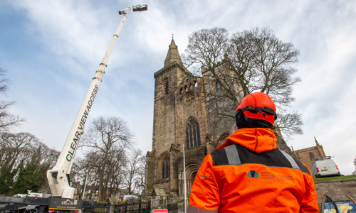 A crane outside Dunfermline Abbey with a man in orange safety clothing overseeing the work