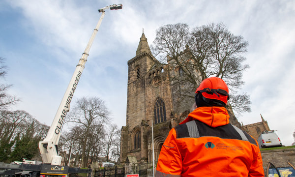 A crane outside Dunfermline Abbey with a man in orange safety clothing overseeing the work