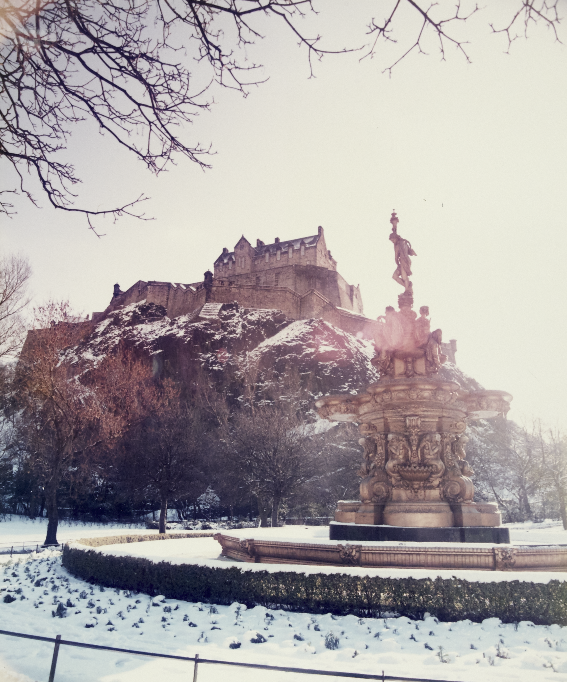 Snowy Prince St gardens fountain with Edinburgh Castle behind it