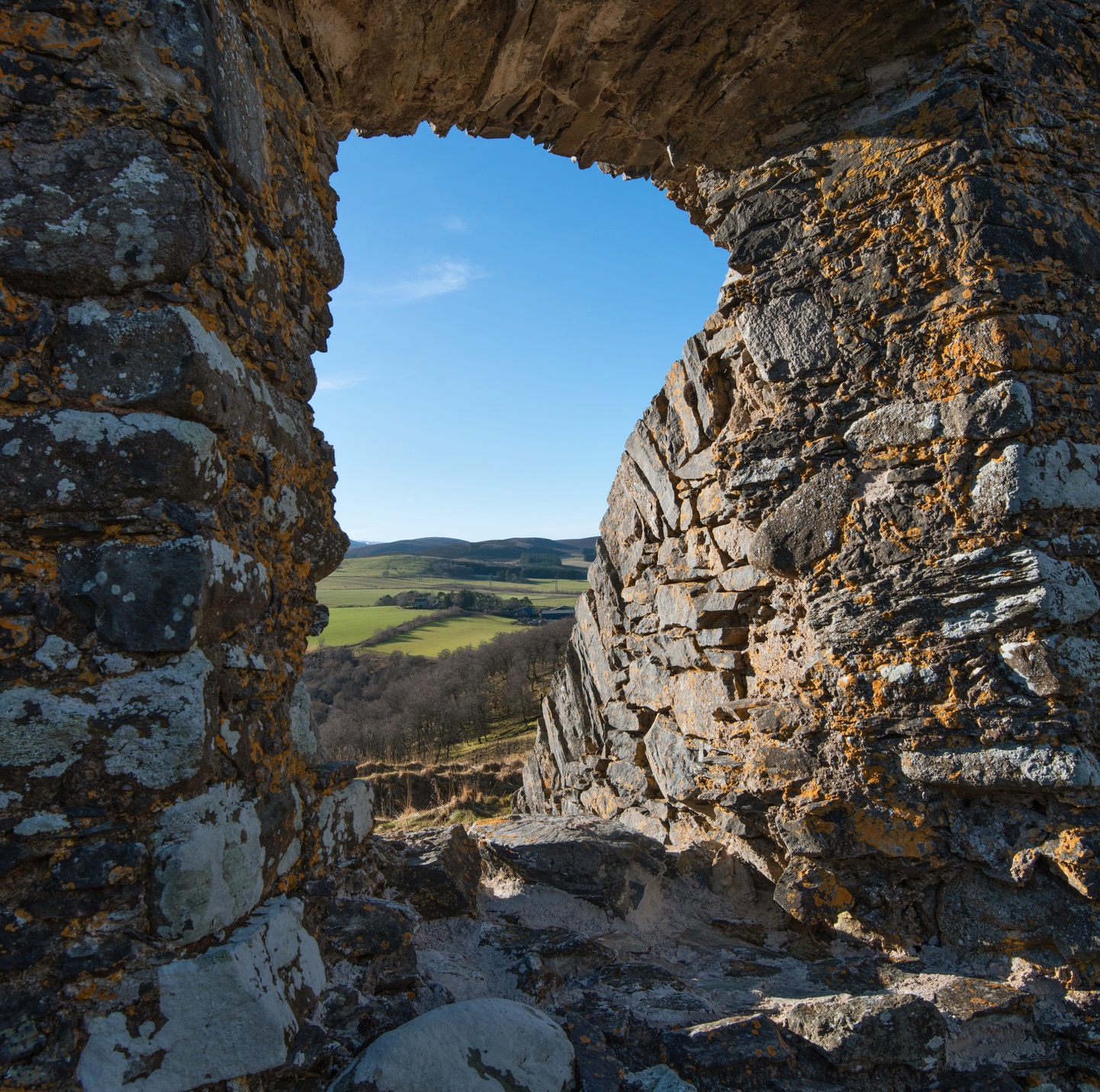 A view through a ruined castle window of farmland and a hills