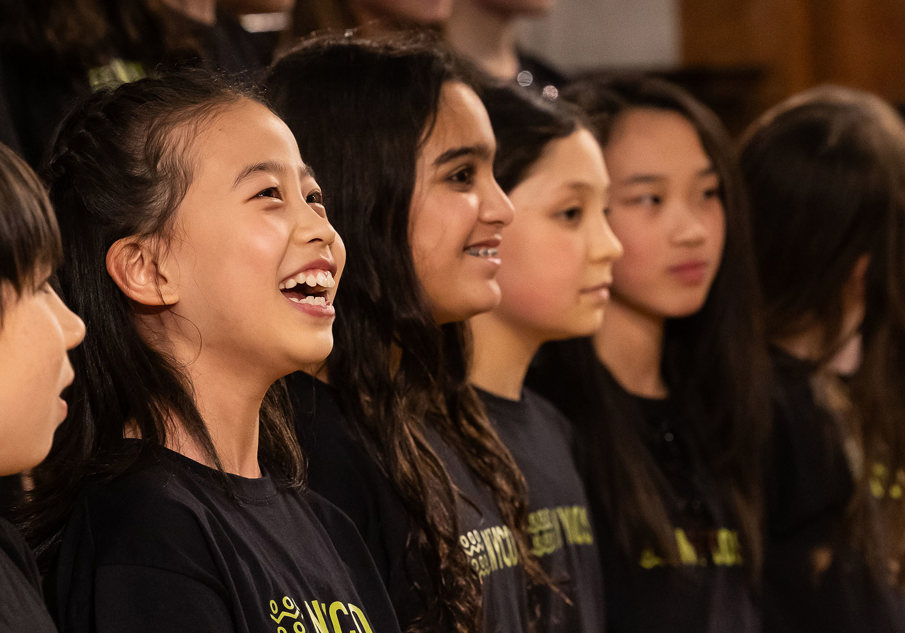 A group of young people wearing tshirts saying NYCOS smiling and singing