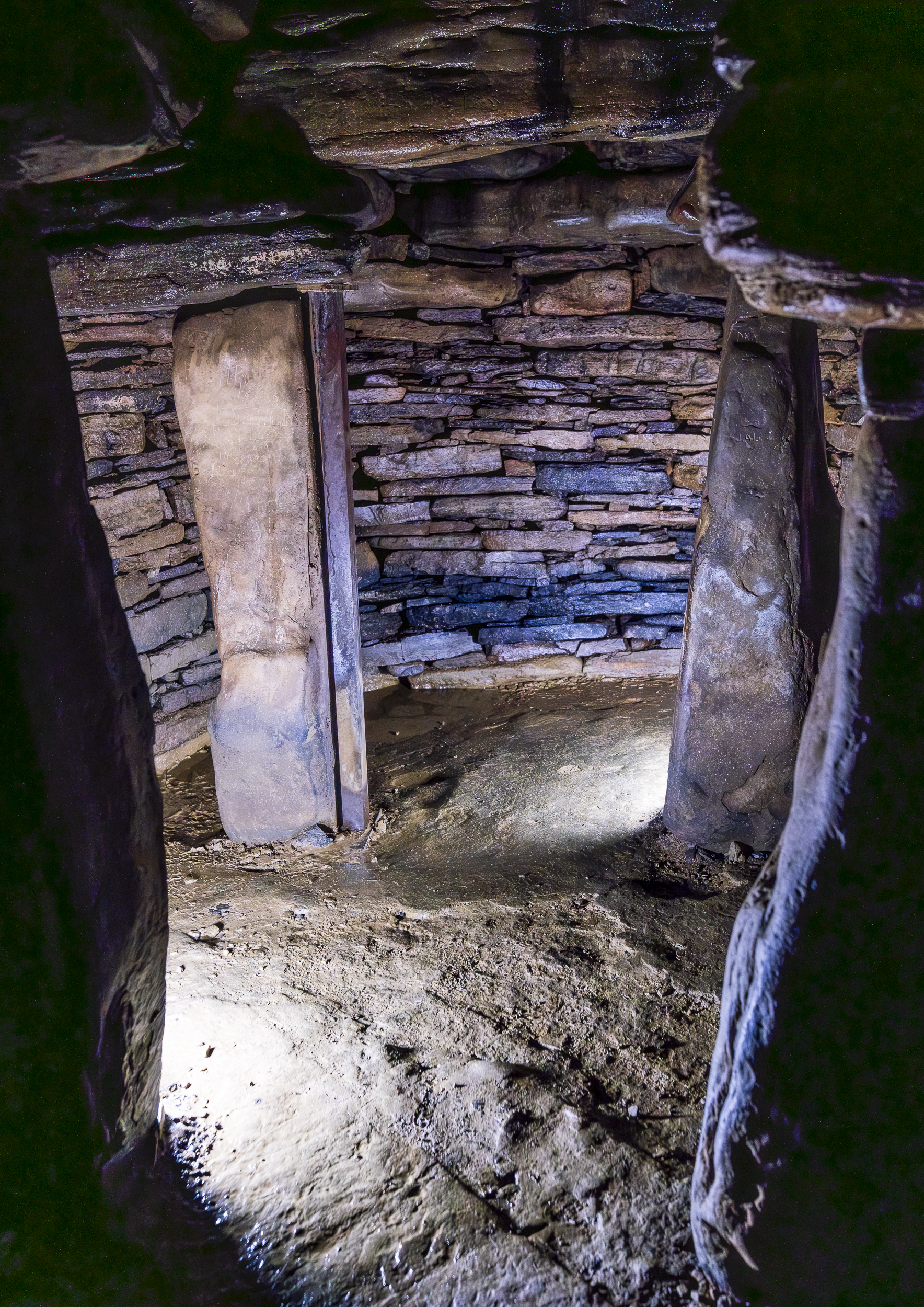 Upright standing stones inside a small, dark chamber with stone walls 