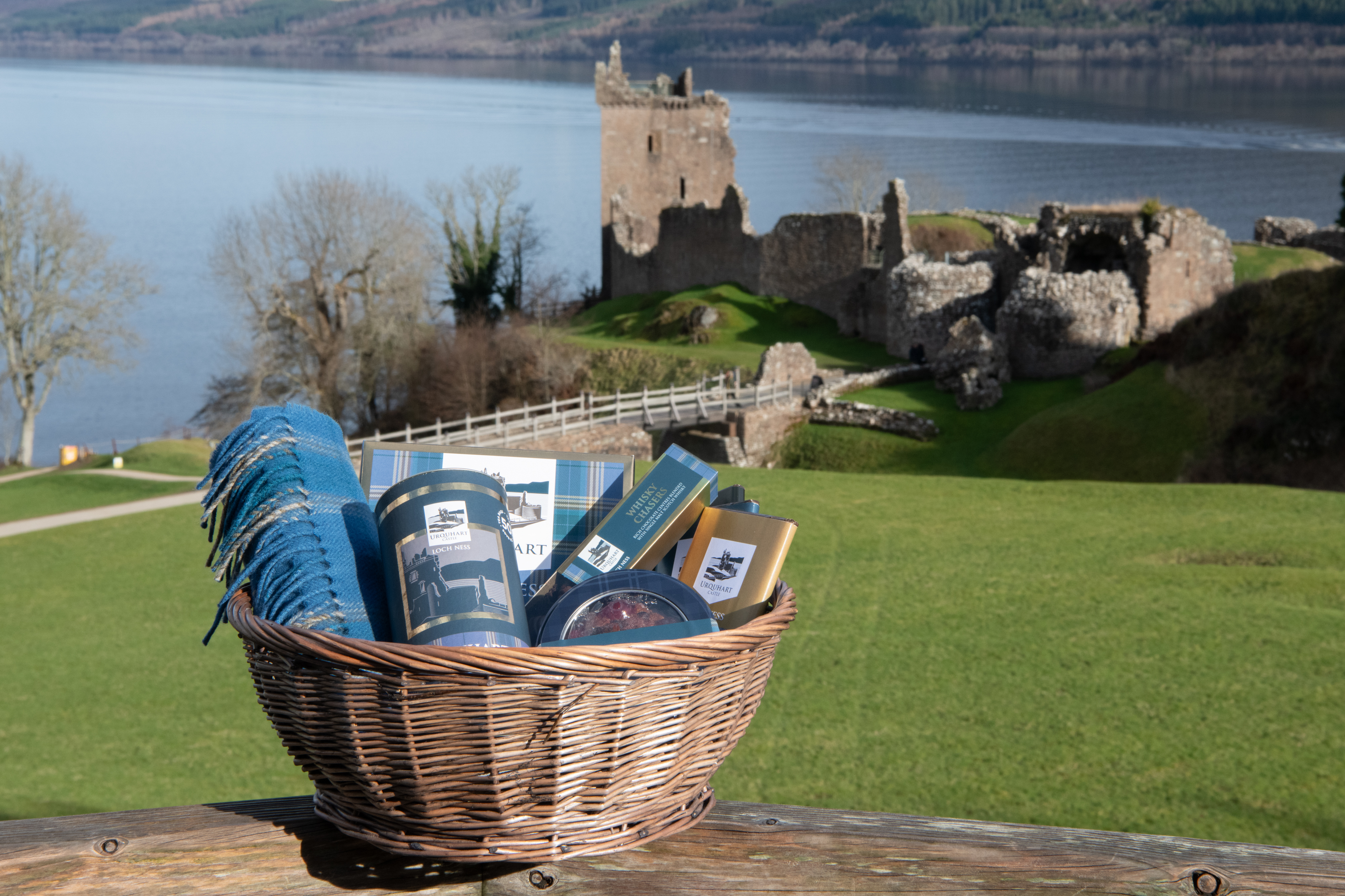Basket of various Urquhart Castle branded gifts with the castle and Loch Ness in the background 