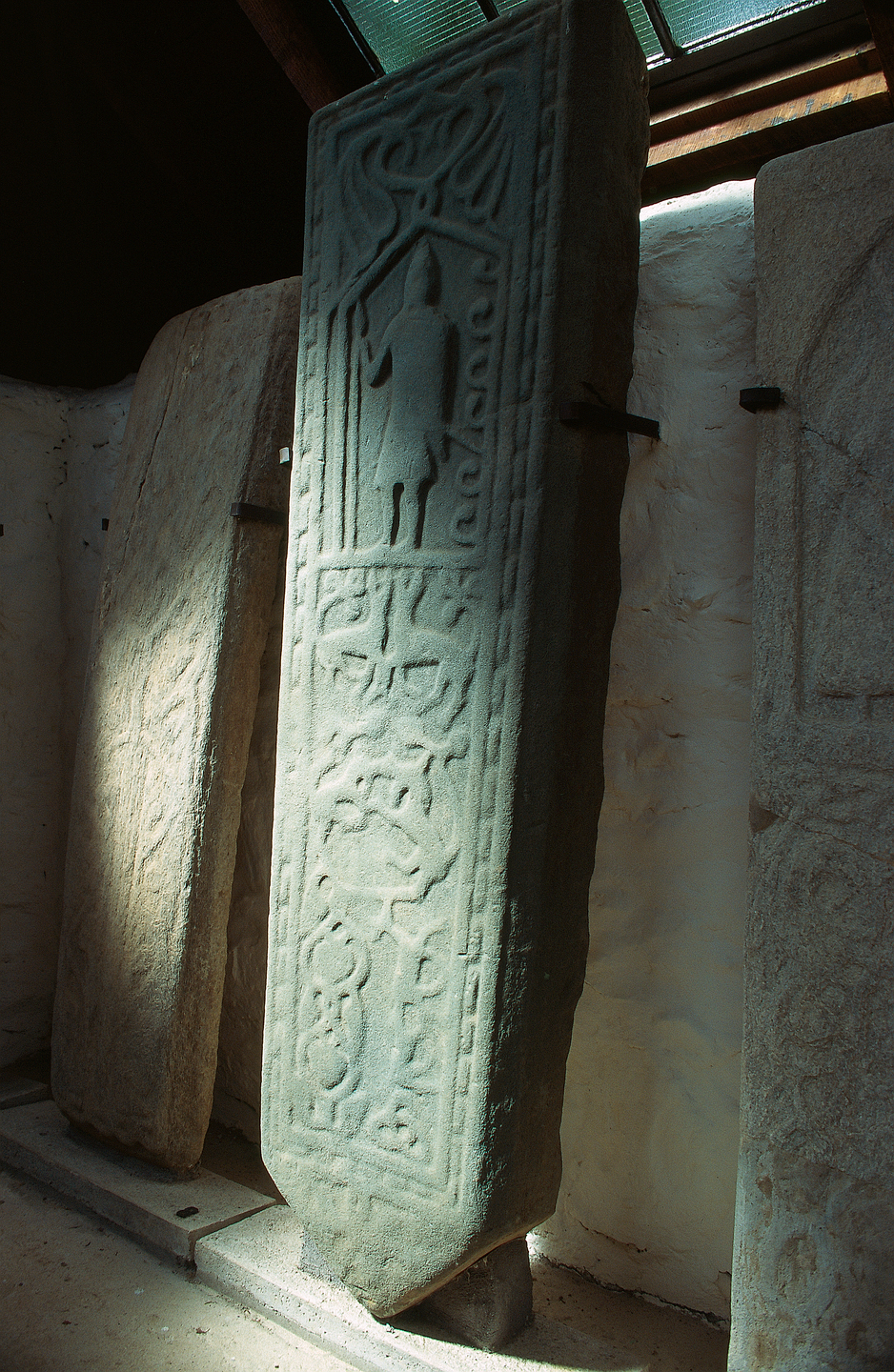 Three sculptured stones standing next to each other. The central stone has a person engraved at the top. It is dark.