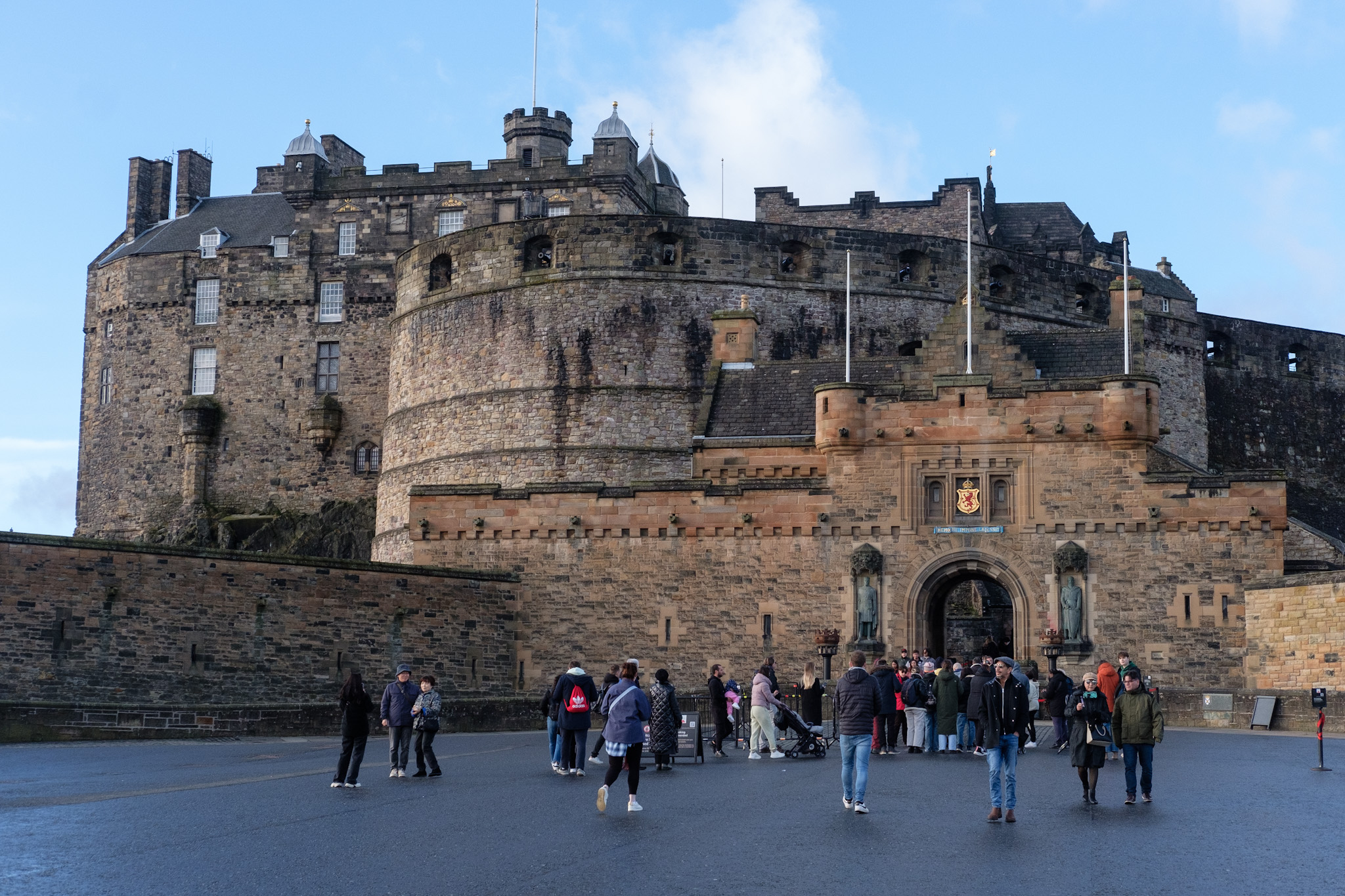 Visitors mill about on the expansive esplanade in front of the imposing walls and entrance to Edinburgh Castle.
