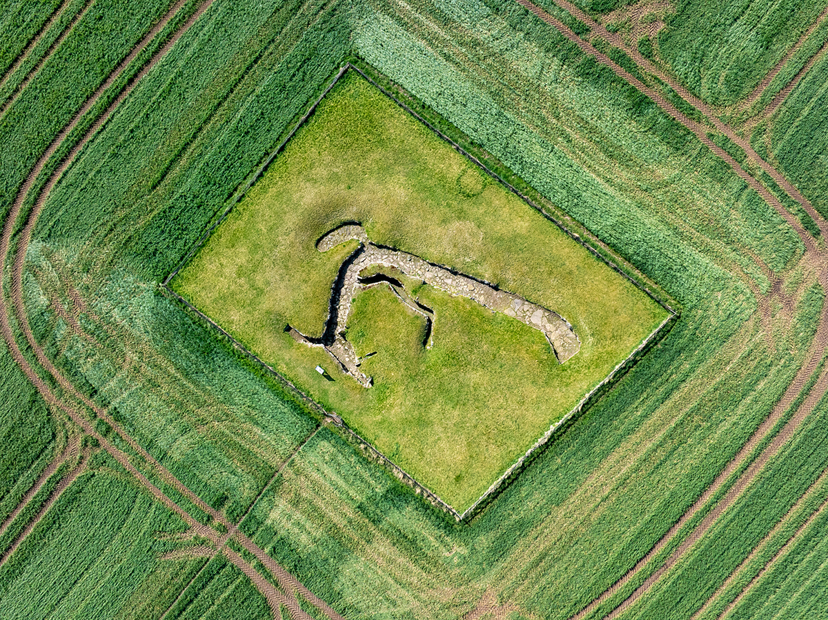 aerial view of grassy field with a large L shape outlined in exposed earth, an earth house used for storage in Iron Age Scotland
