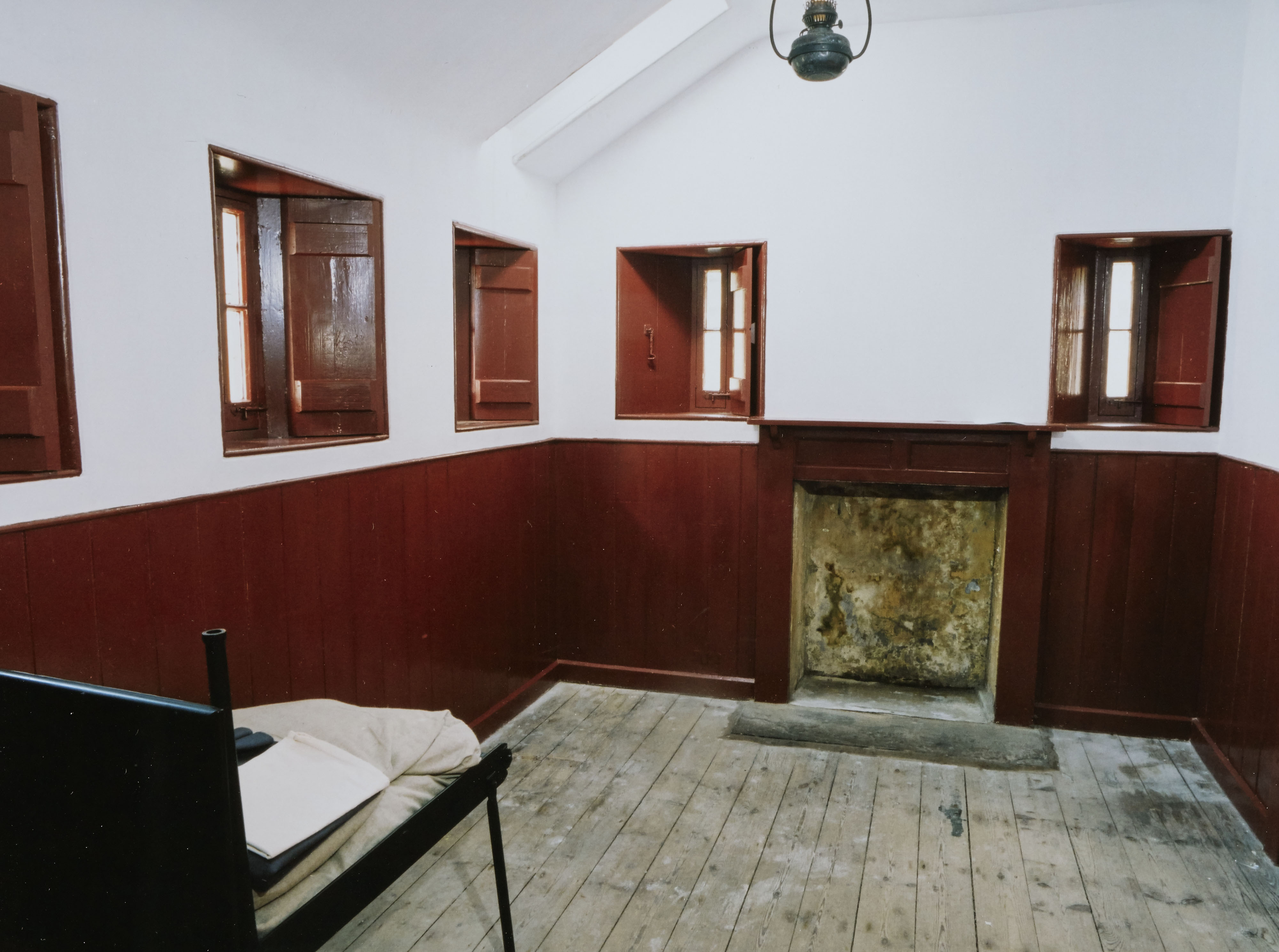 A room with a wooden floor and red and white walls, with a mantlepiece build into the walls and five small windows