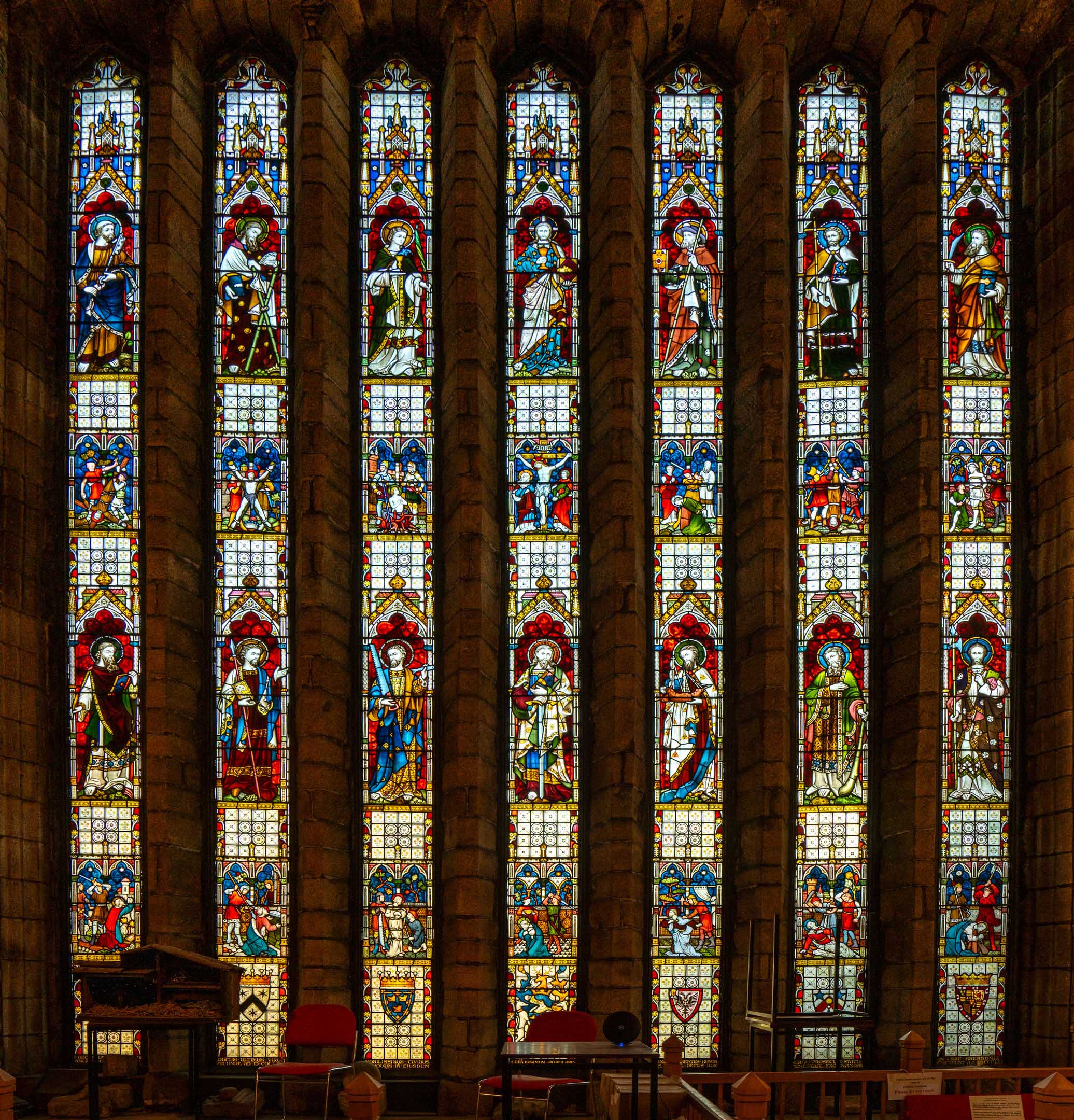Tall stained-glass window with multiple panels of saints set within stone columns.