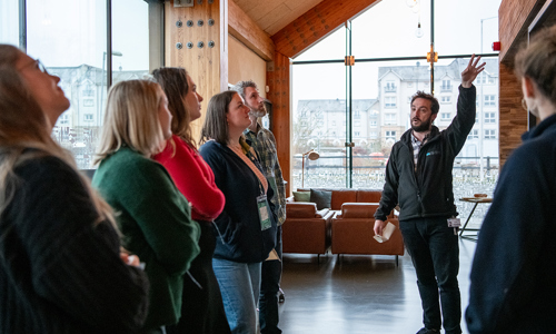 A group of people inside one of the glass wings of the Engine Shed building. One person has their hand raised and is giving a talk to the rest of the group.