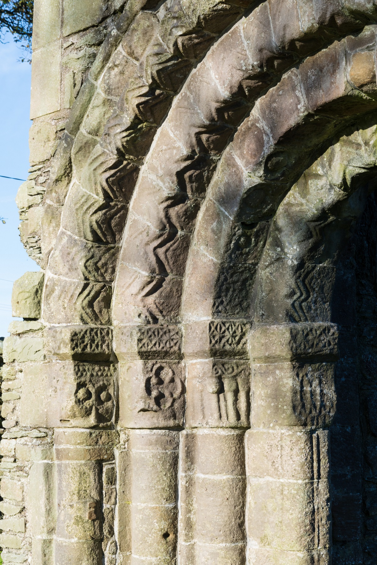 Close-up of carved stone arche at Whithorn Priory, showing zigzag and geometric Romanesque decoration on weathered sandstone columns.